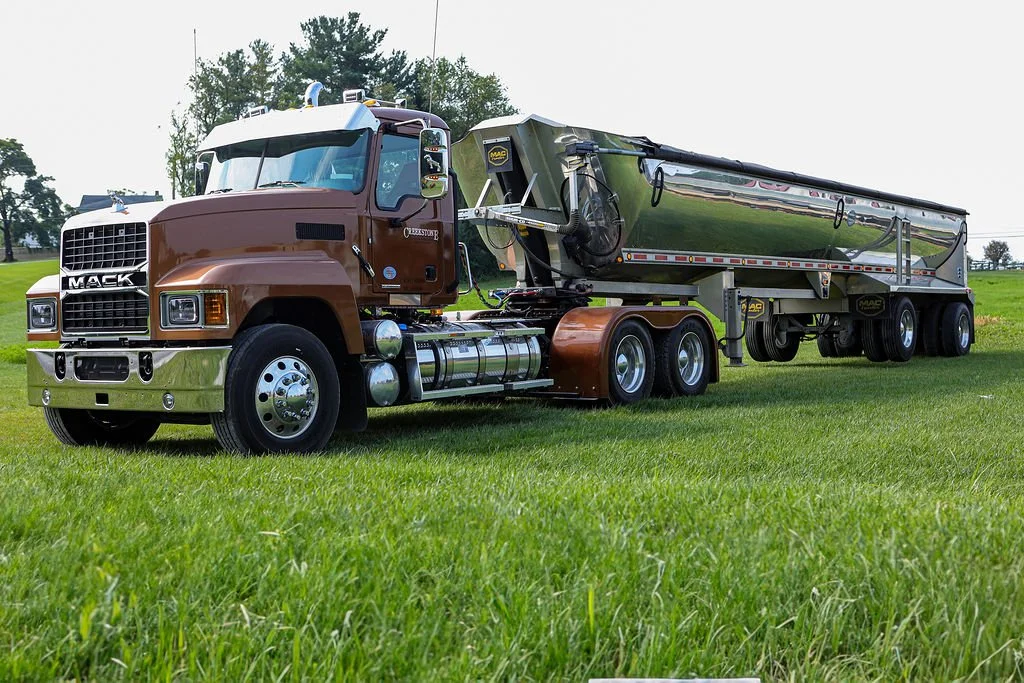 Creekstone brown-cab truck with a shiny metallic trailer parked on a grassy field, showcasing heavy-duty trucking and hauling capabilities.