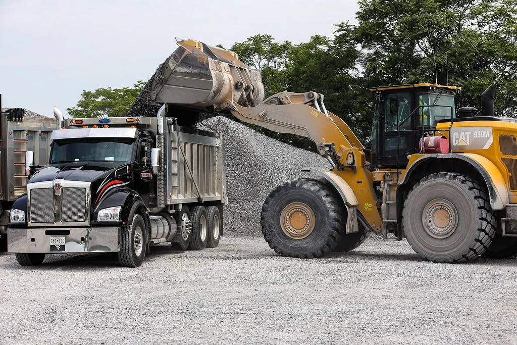 Creekstone Caterpillar front loader dumping gravel into a dump truck on a gravel lot, highlighting heavy equipment operation and material hauling services.