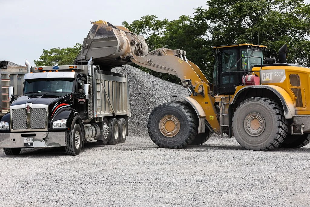 Creekstone construction vehicle loading gravel into a dump truck at an active construction site, highlighting heavy equipment operation and material hauling services.