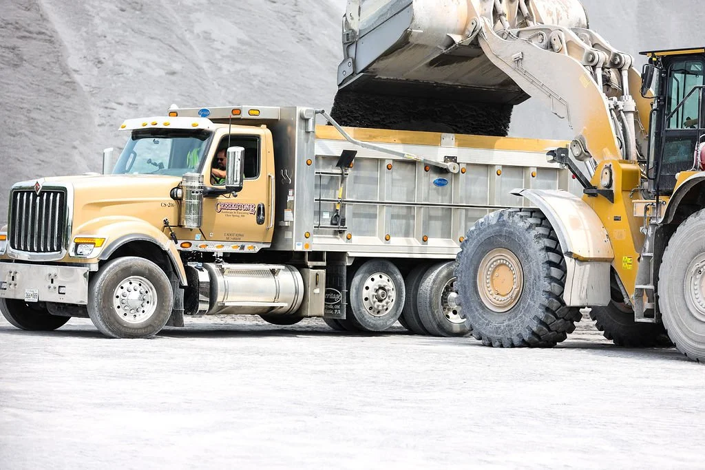 Creekstone construction site with a yellow dump truck and a large front loader moving dirt and gravel, highlighting excavation and material handling operations.