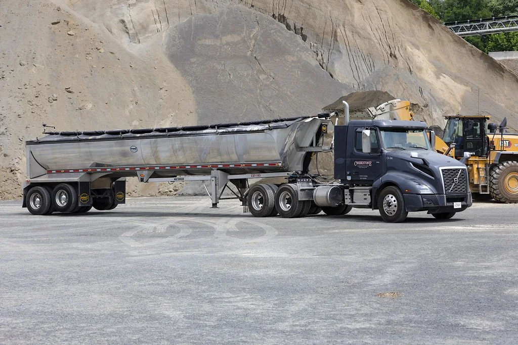A Creekstone large semi-truck with a tanker trailer parked on a construction site or quarry, with a dirt hill and construction equipment in the background.