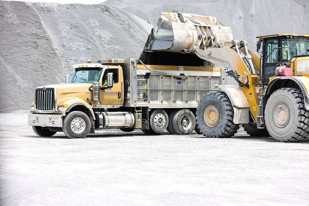 A large construction vehicle, a dump truck, distributing material into a wheel loader at a mining or construction site.