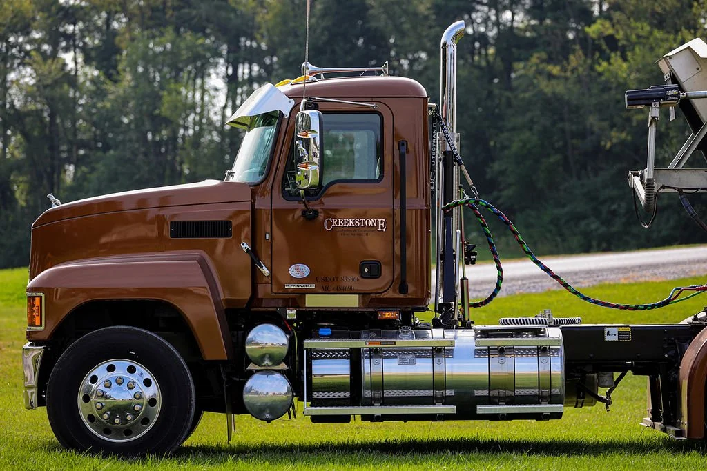 Creekstone brown truck parked on a grassy field with trees in the background, highlighting heavy-duty trucking and hauling capabilities.