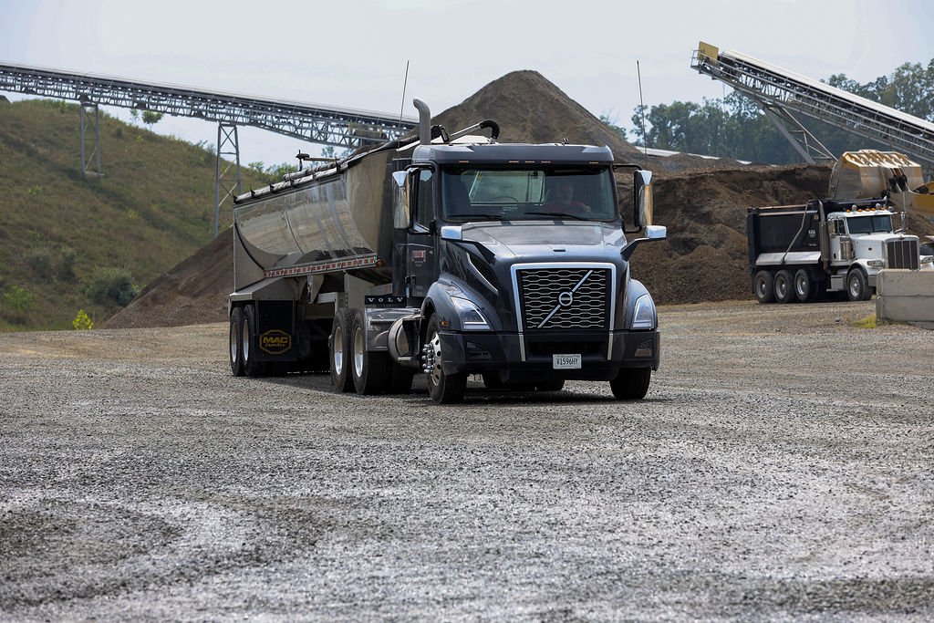 Creekstone black semi-truck parked in a gravel industrial yard with dirt piles and construction equipment in the background, highlighting heavy hauling and construction site operations.