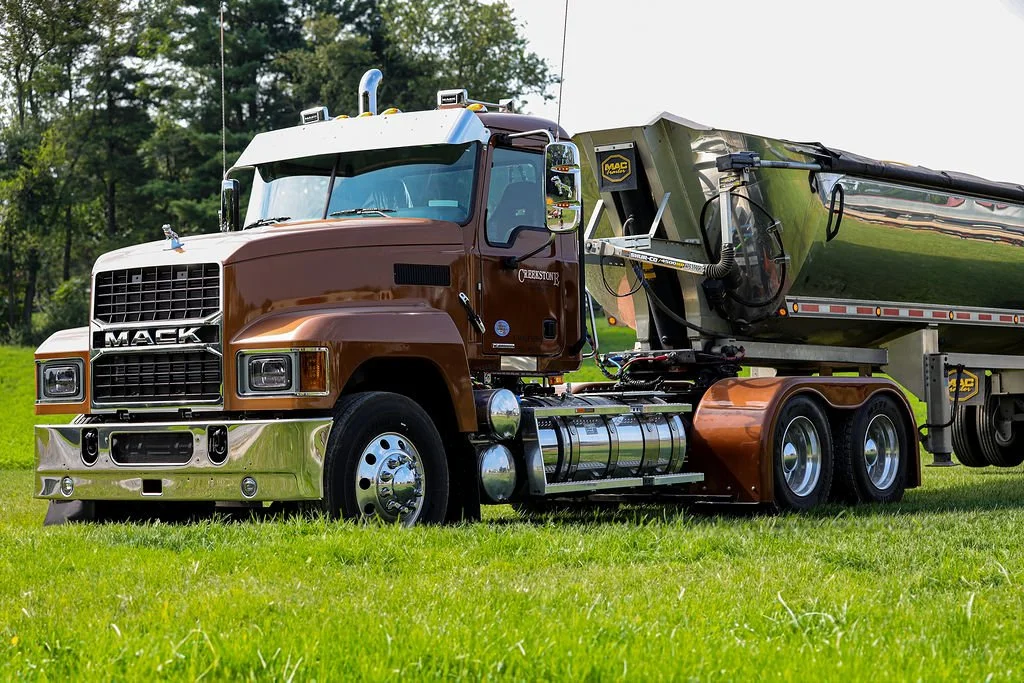 Creekstone Mack hauling truck parked on a grassy field with trees in the background, highlighting heavy-duty trucking and hauling services.