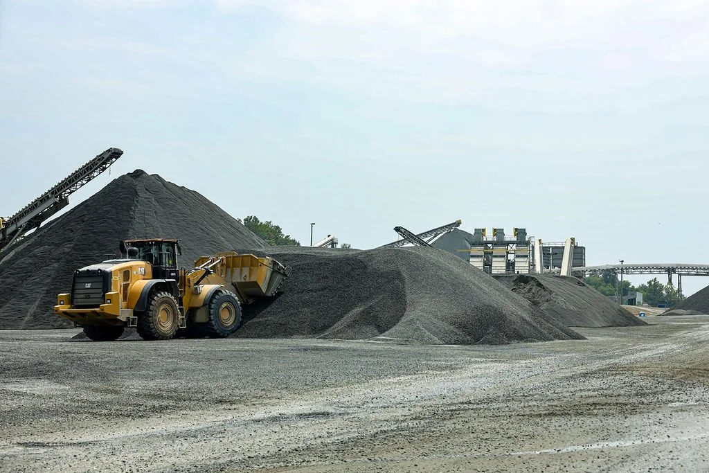 A construction site with piles of gravel, a large yellow front loader, and industrial equipment in the background.