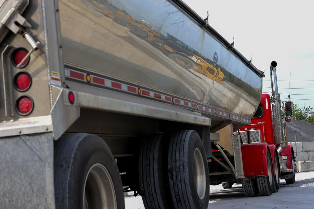 Creekstone red semi-truck with a reflective chrome side panel parked on a gravel surface with concrete blocks in the background, highlighting heavy-duty trucking and material transport services.