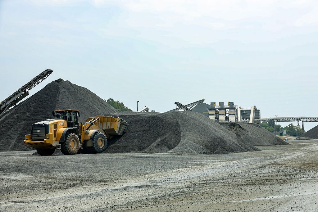 Creekstone construction site with gravel piles, a yellow loader, and industrial conveyor belts, showcasing aggregate processing and heavy equipment operations.