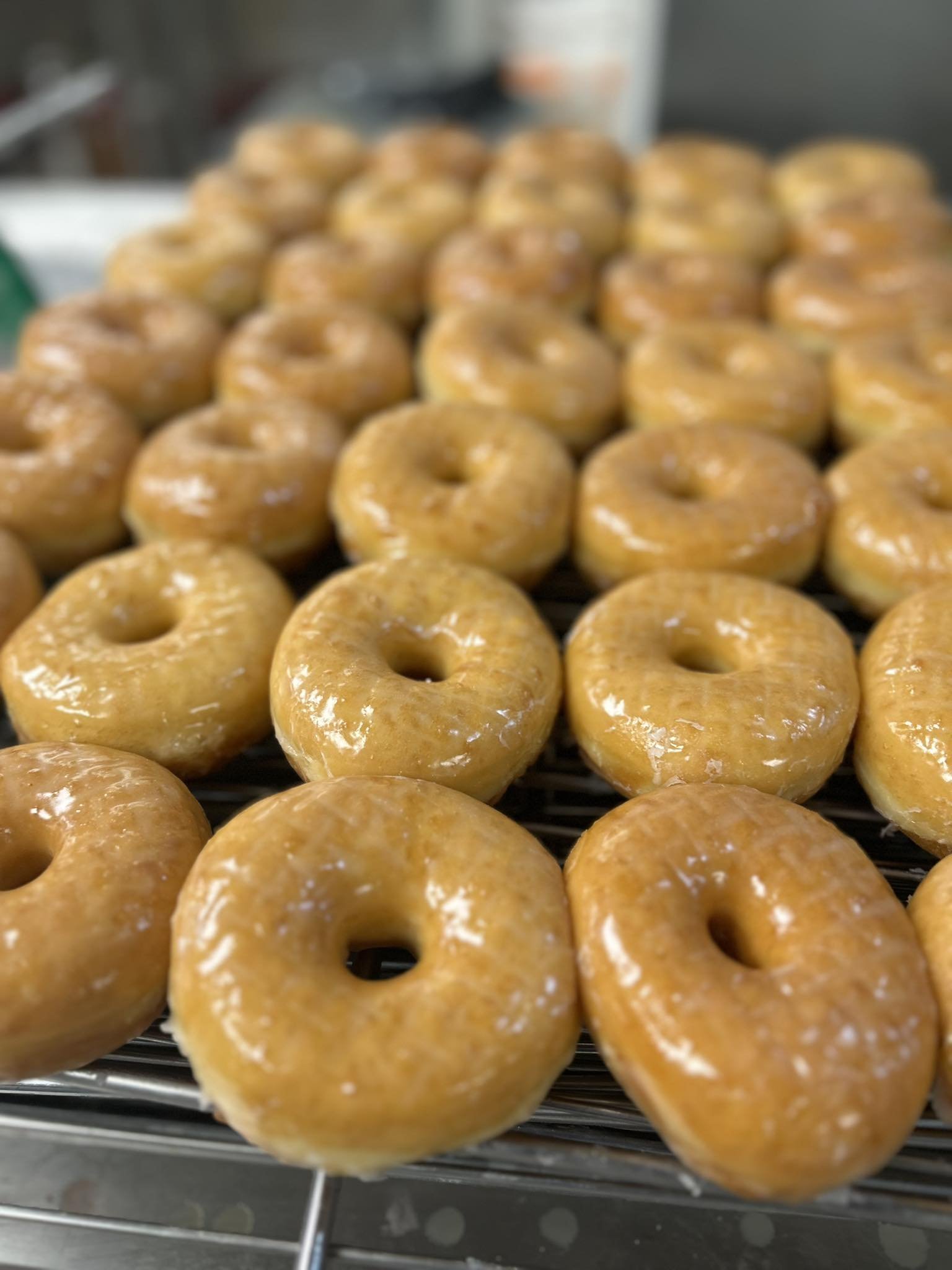 Multiple donuts sit next to each other. They are all round with a hole, light brown in color and shiny with glaze