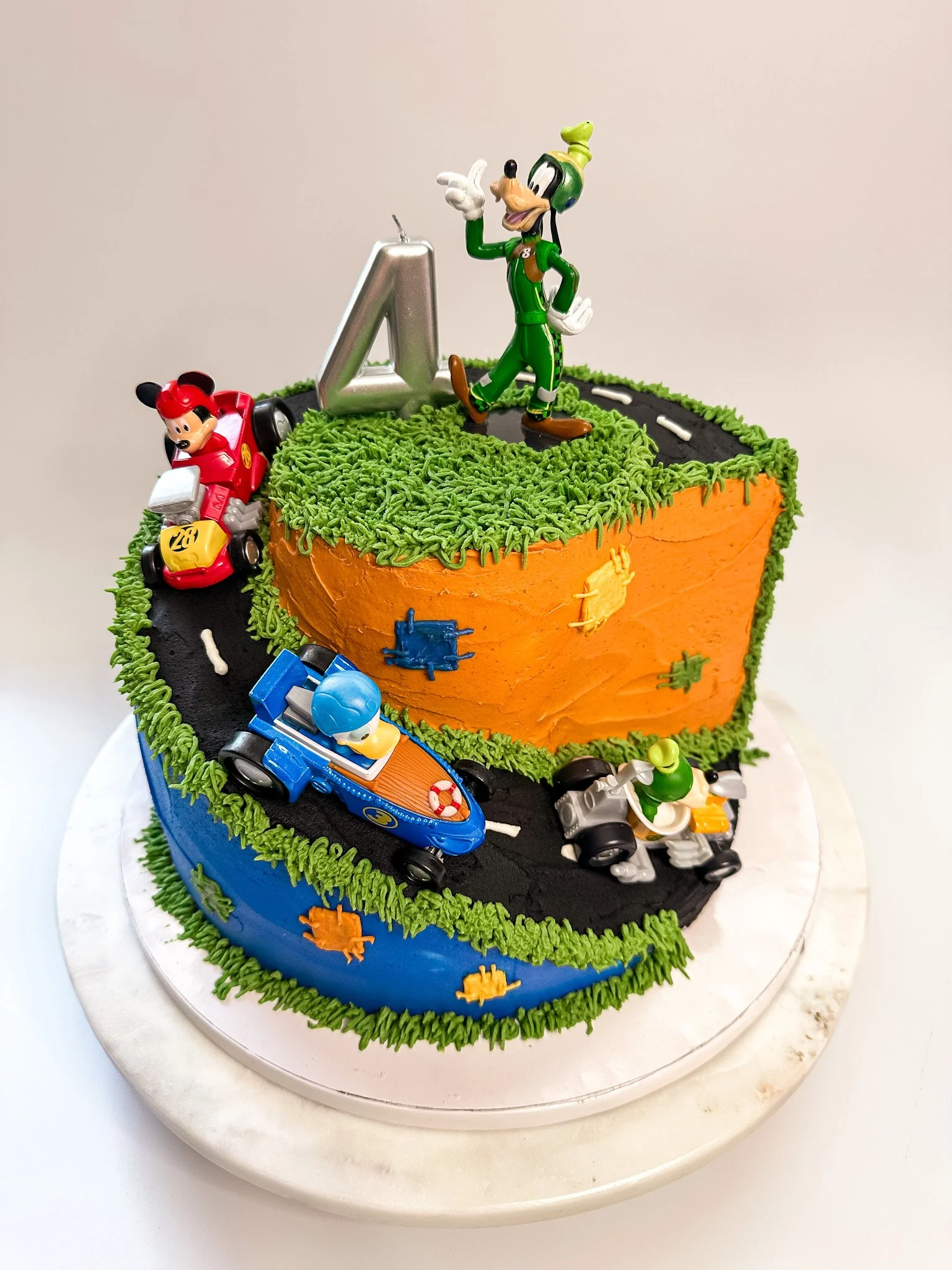 Race car themed birthday cake with Toy Story characters and a large number 4 cake topper, decorated with colorful icing and edible decorations.