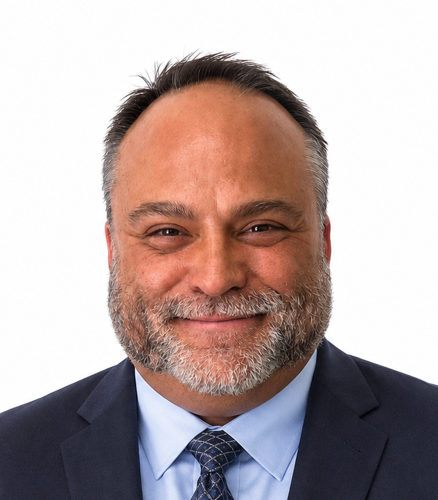 Close-up of a middle-aged man with short gray hair and a beard, smiling, wearing a light blue collared shirt with a logo on the chest.