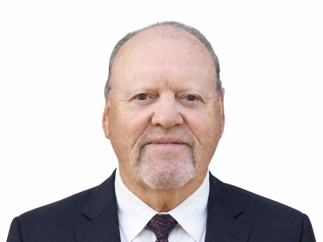 Close-up portrait of an older man with a bald head, light beard, and wearing a peach-colored collared shirt.