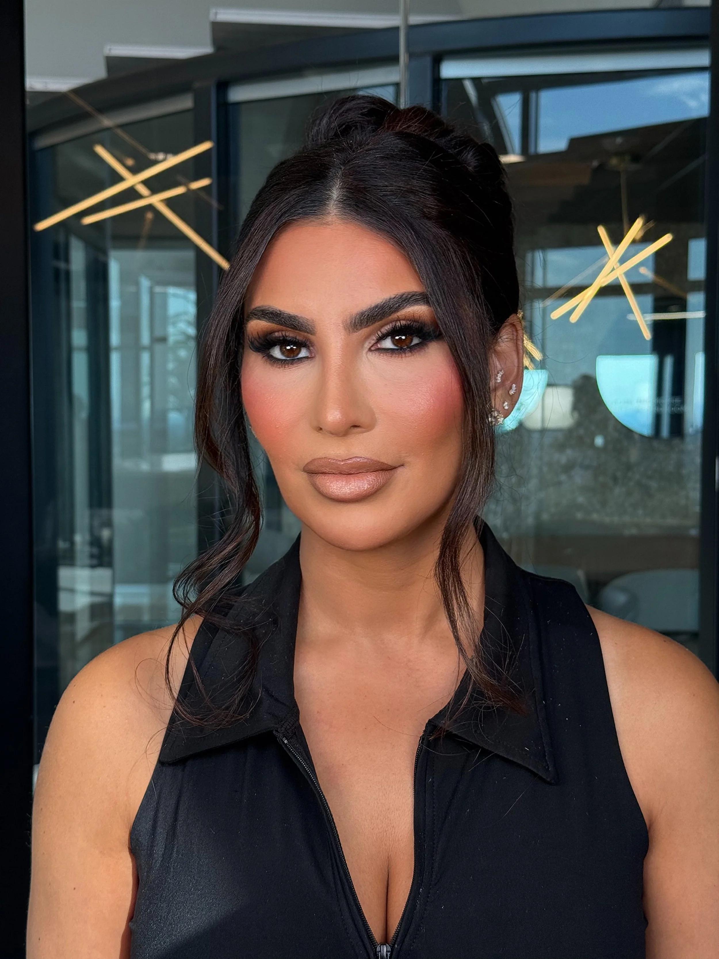 Professional event makeup and hairstyling with loose waves on a client in a modern Dallas indoor setting.