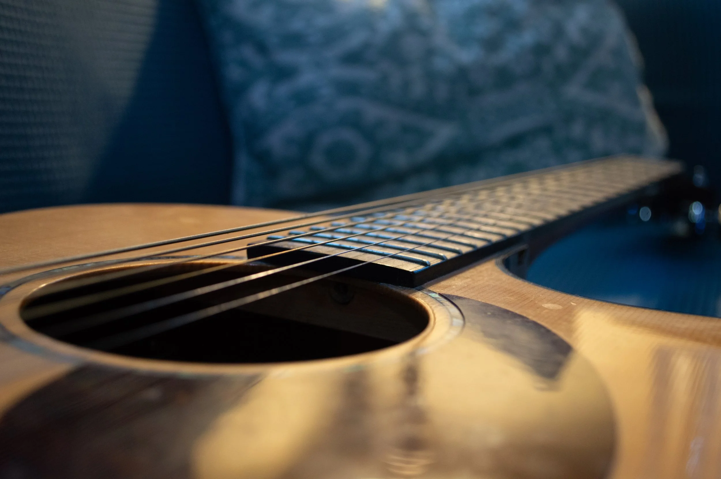 Close-up of an acoustic guitar resting on a person's lap, with a blurred fabric background.