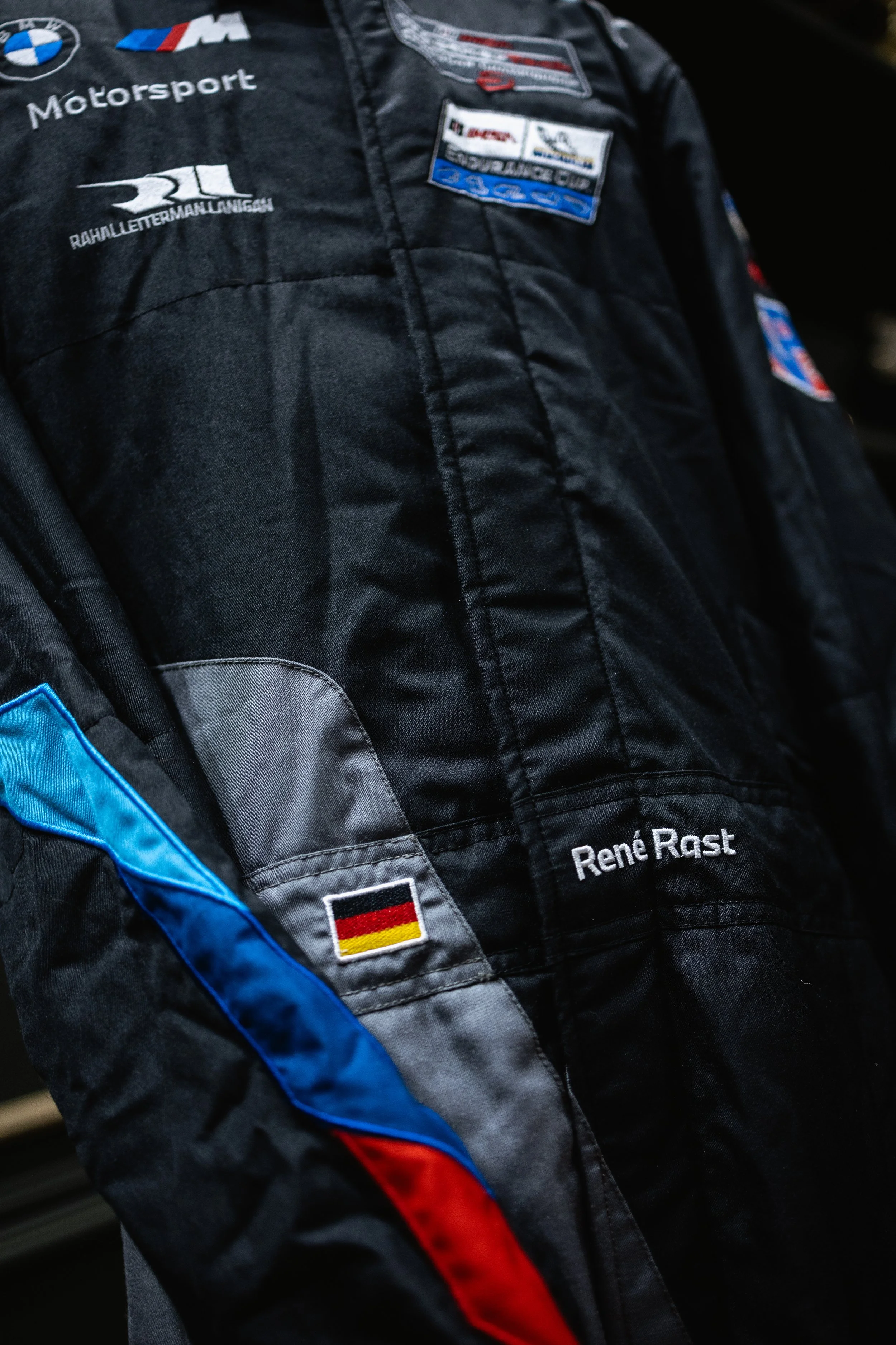 Close-up of a racing suit with patches, including a German flag, BMW Motorsport, and the name Rene Rast.