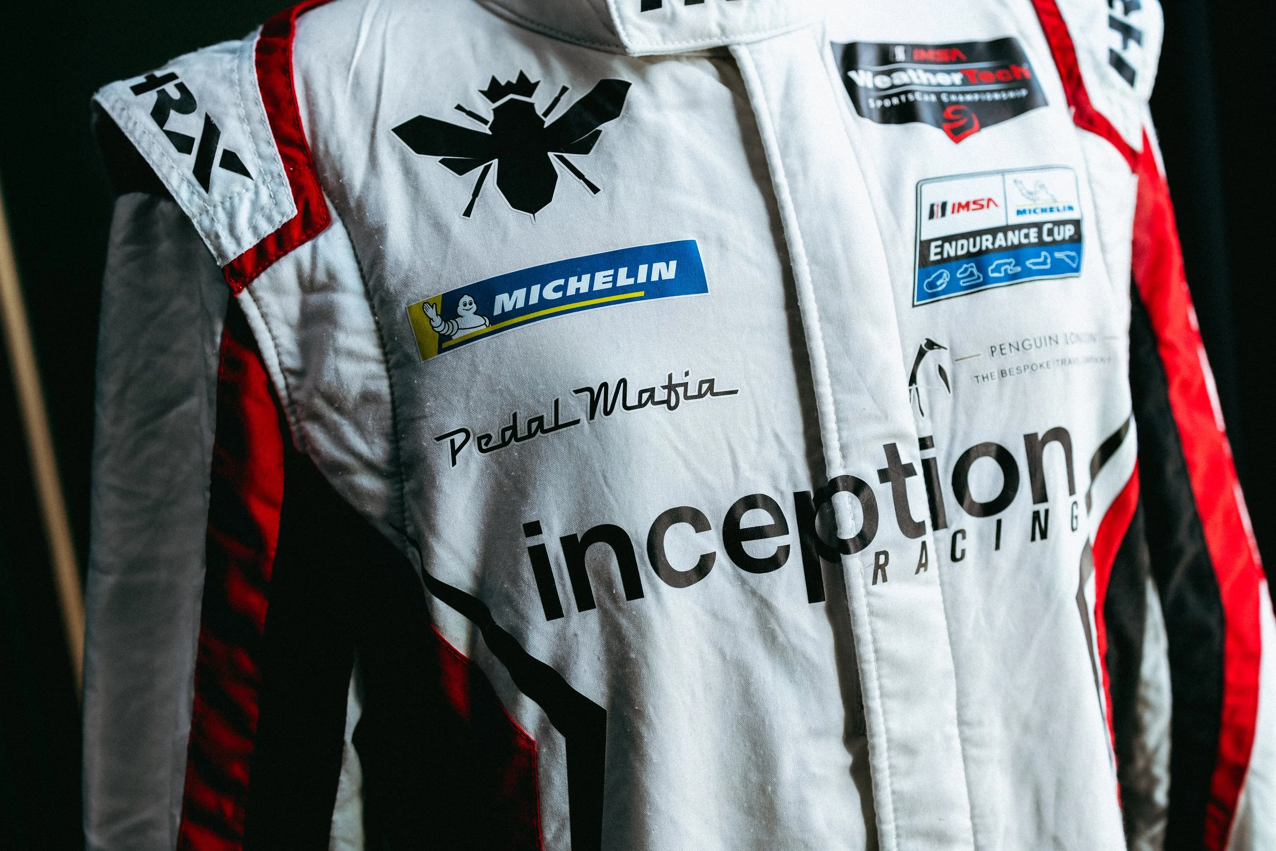 Close-up of a racing suit with various sponsor logos, including Michelin, Pedal Mafia, Inception Racing, and others.