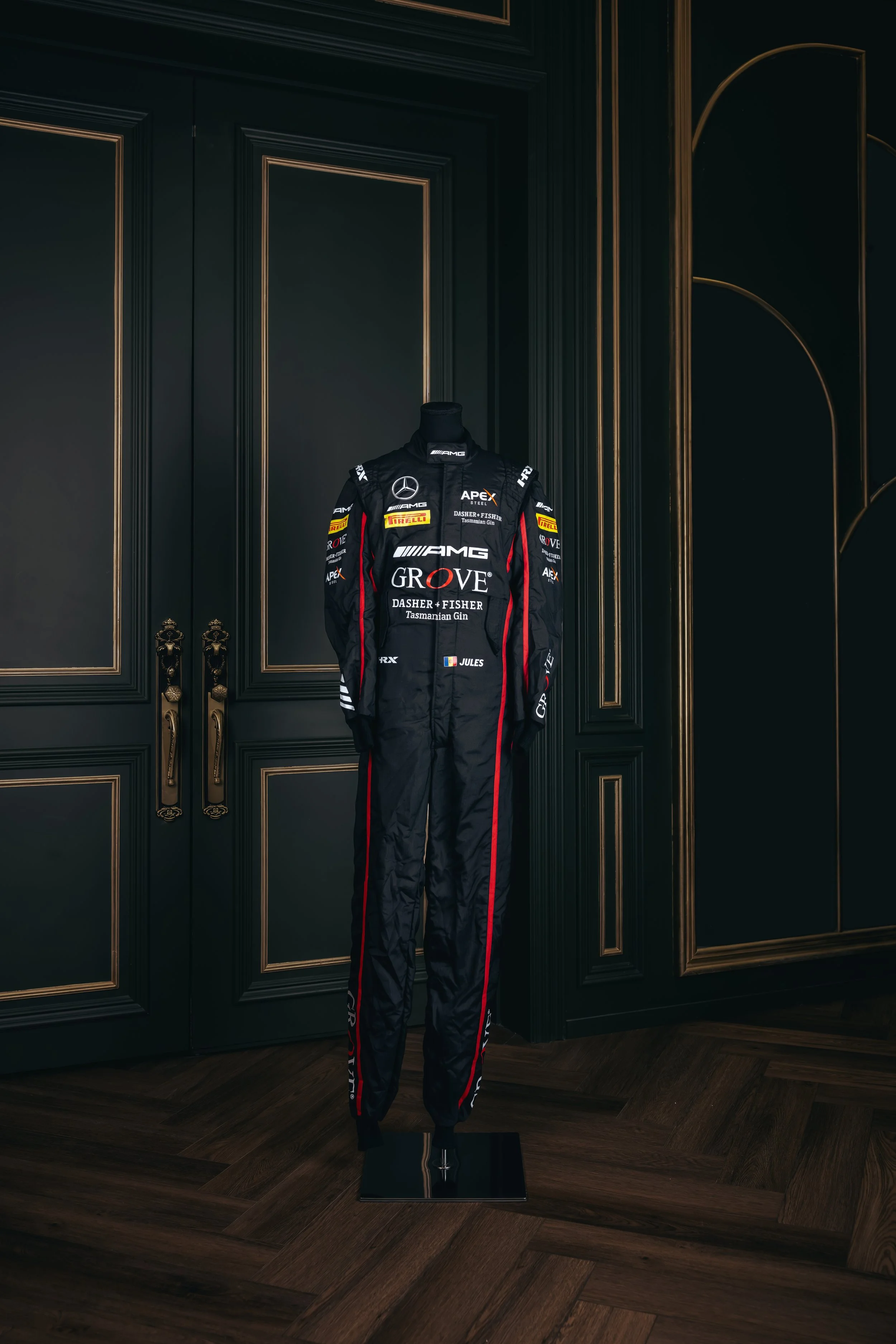 A racing suit displayed on a mannequin against a dark, ornate wooden wall in a room.