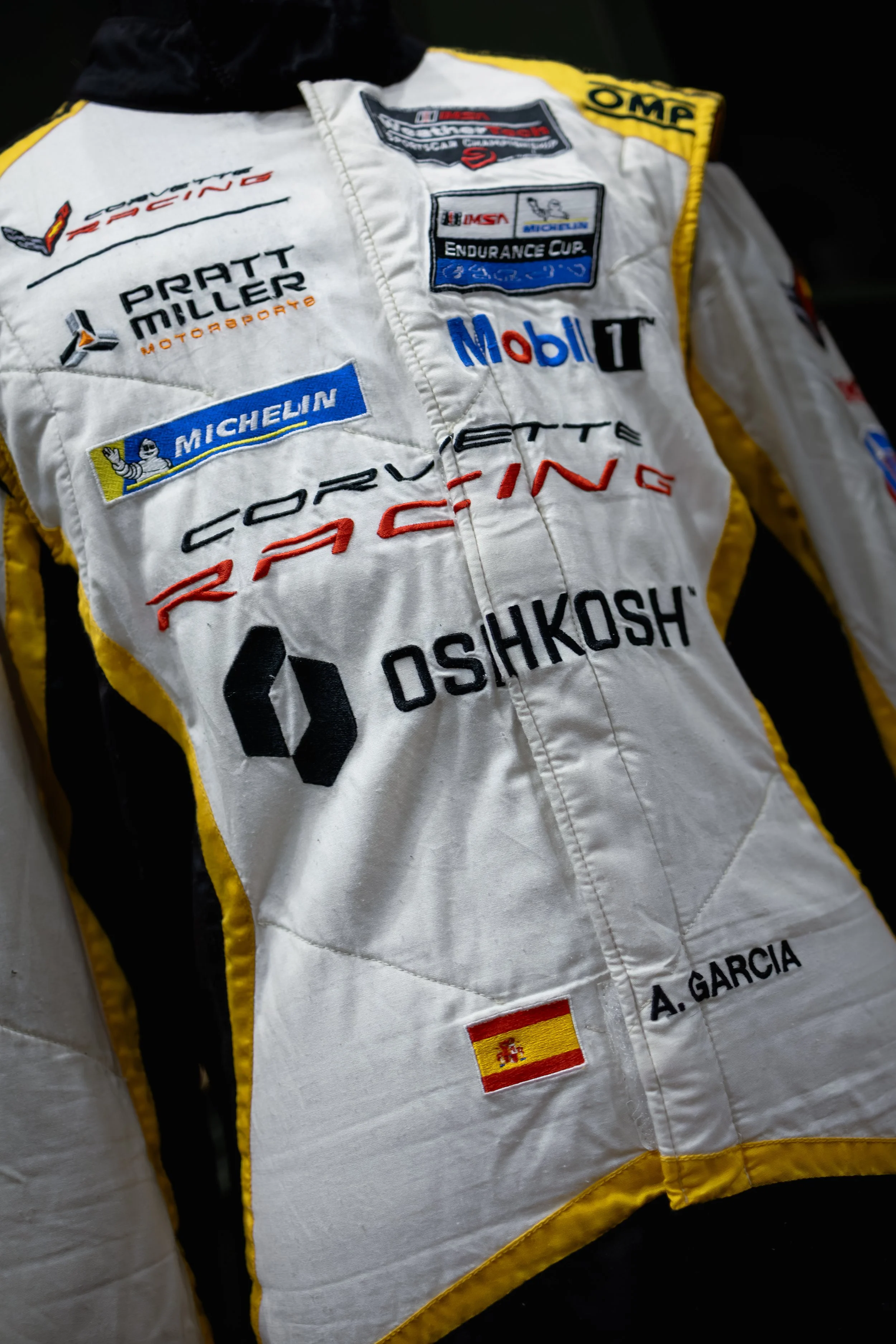 Racing suit with various sponsor patches including Michelin, Mobil, and OshKosh, and the name A. Garcia with a Spanish flag patch.