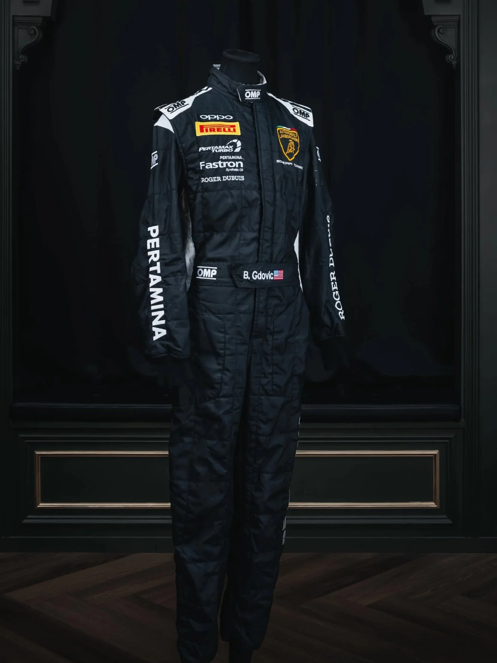 A racing racing suit on a mannequin, featuring sponsor logos and a Lamborghini emblem, displayed against a black background.