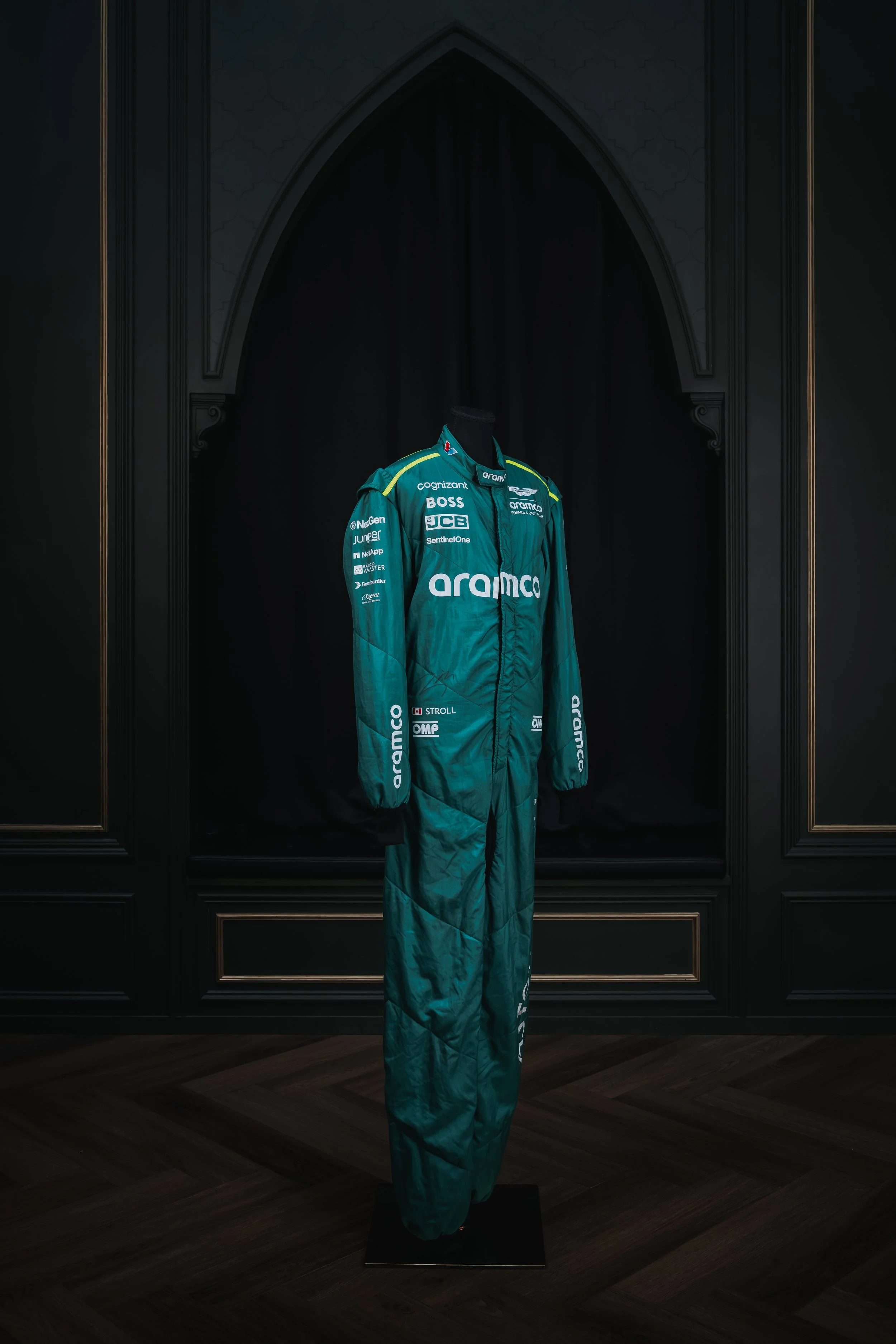 A racing suit on a mannequin, displayed against a dark background with gold accents.