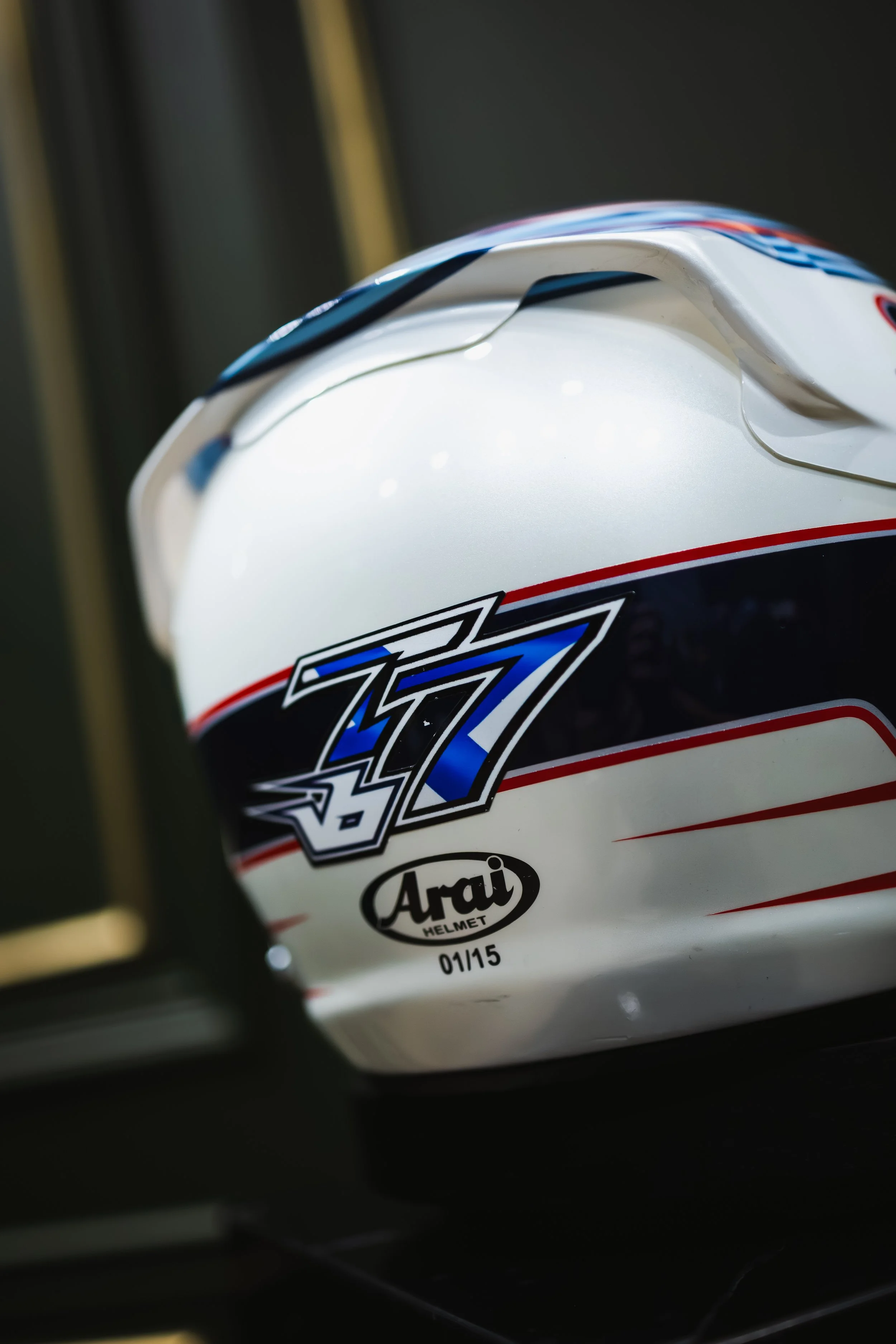 Close-up of a white racing helmet with the number 77 and the Arai logo.