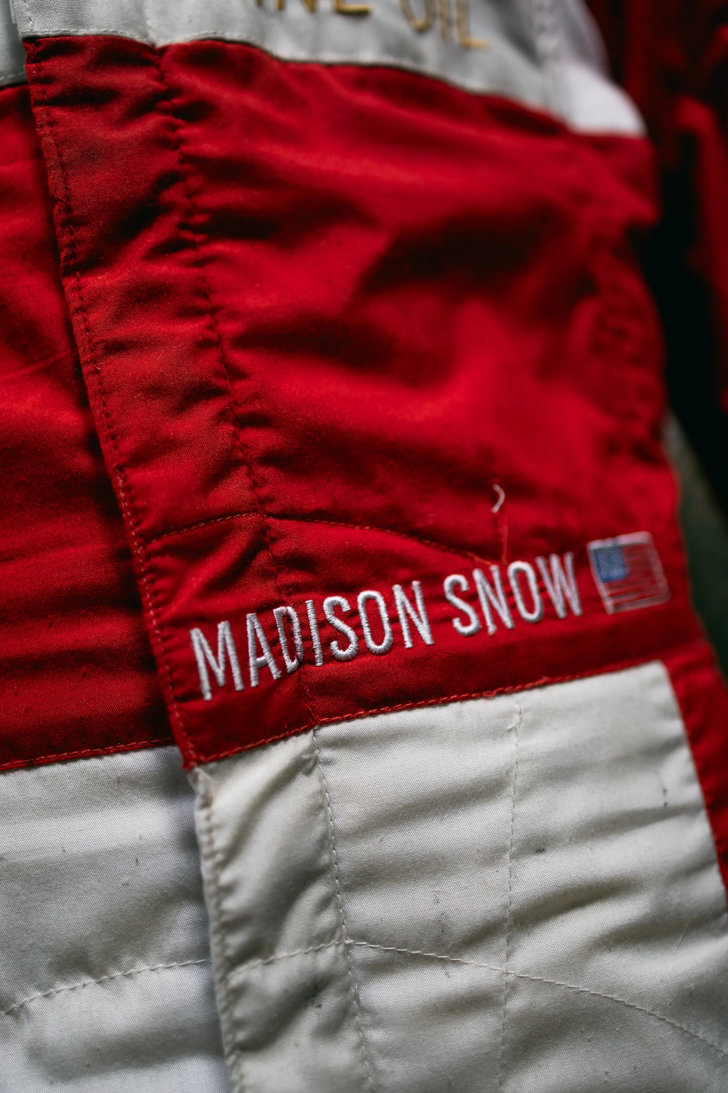 Close-up of a quilted fabric with red and white sections, featuring embroidered text 'MADISON SNOW' and a small American flag patch.