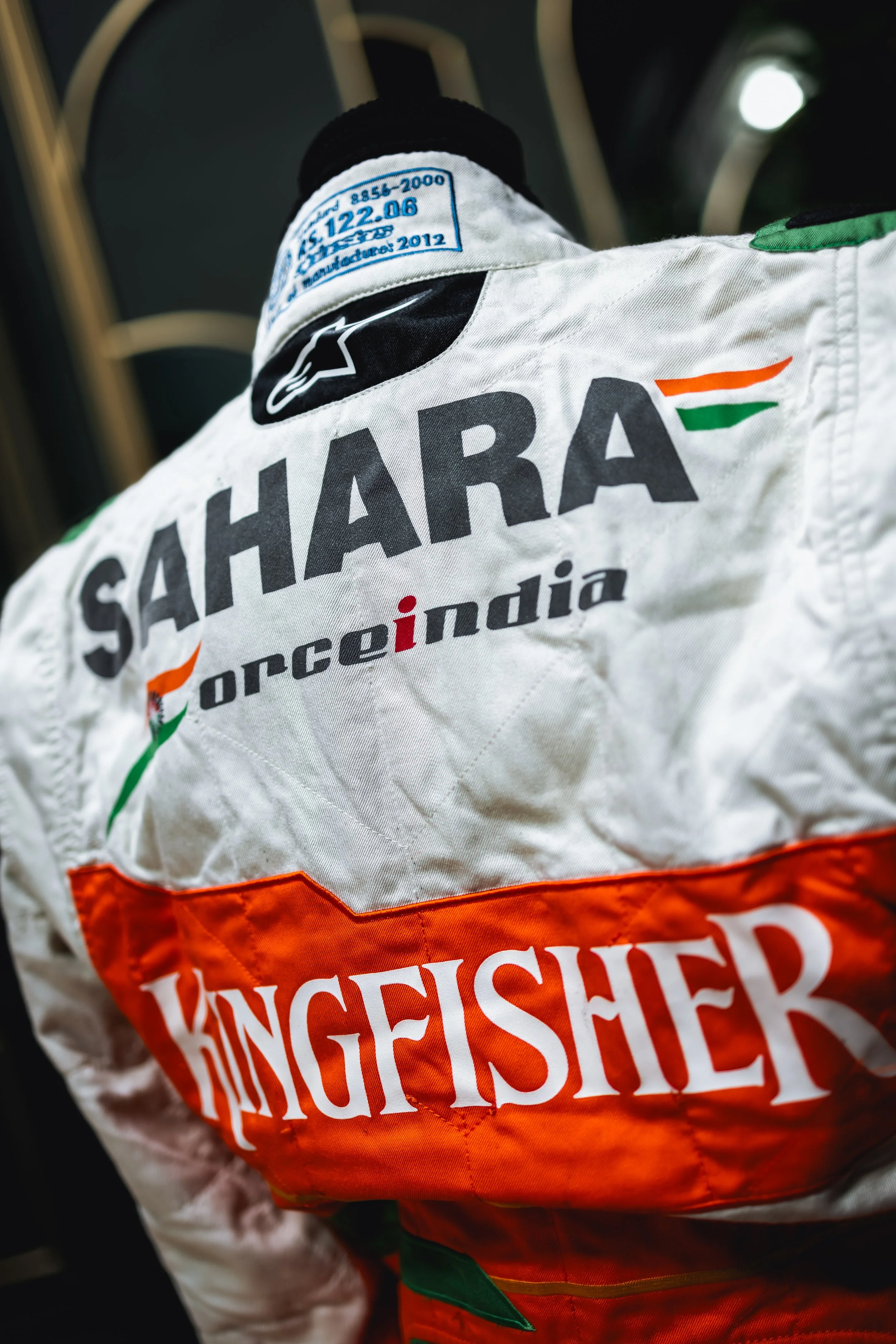 Close-up of a racing suit with the name 'SAHARA' and the logo of Kingfisher beer, featuring Indian colors and the word 'India' on the back.