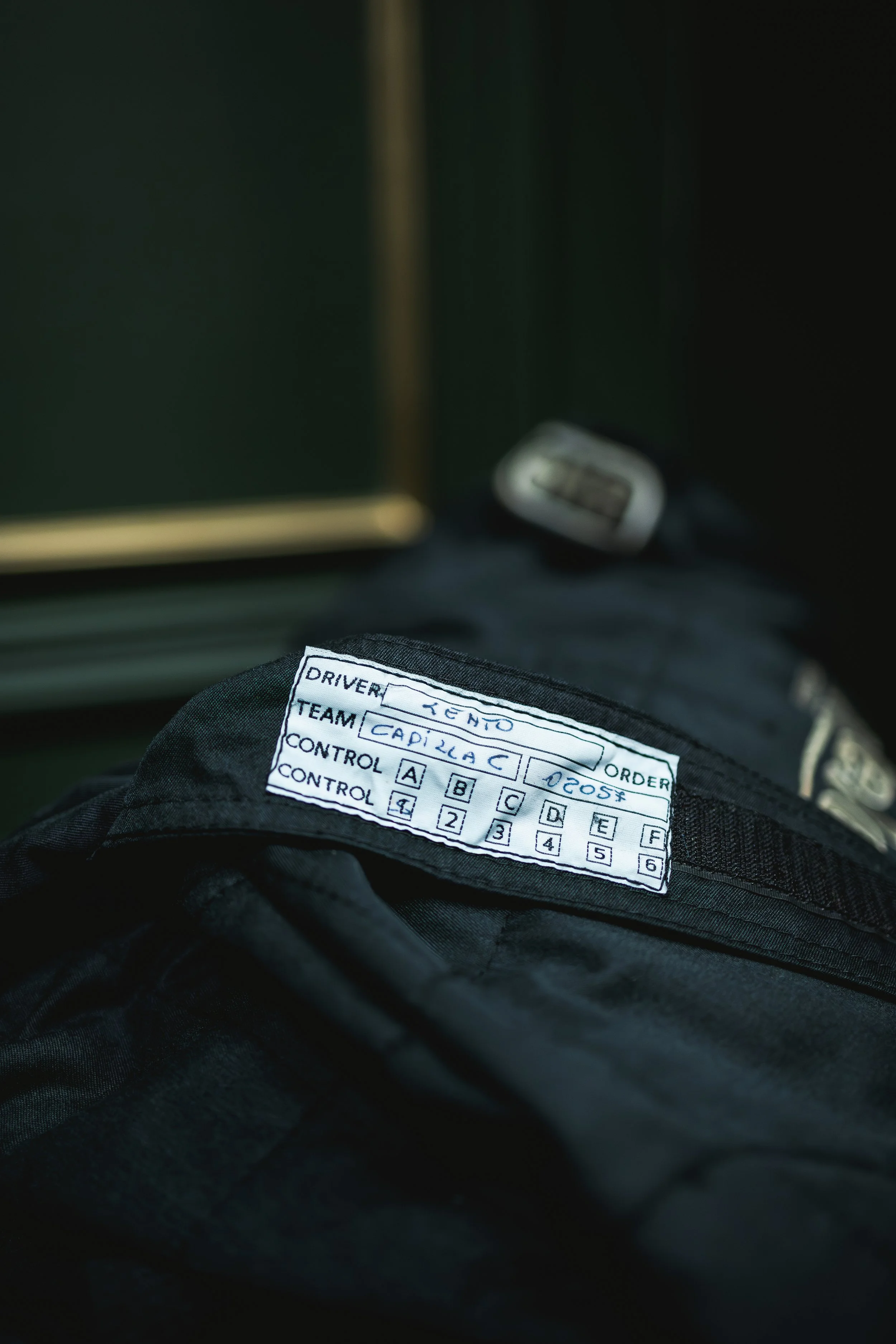 Close-up of a race car driver's uniform with a control sheet showing the driver name 'ZENO', team 'CADA LAC', and controls labeled from A to F, with a blurred background.