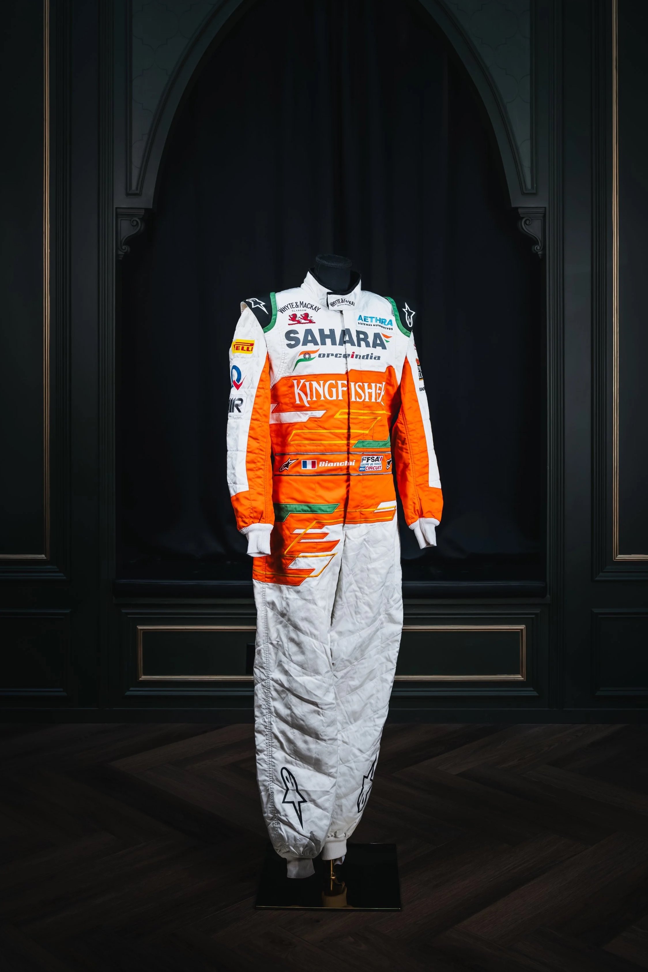 Young male race car driver in racing suit with arms crossed, facing forward.