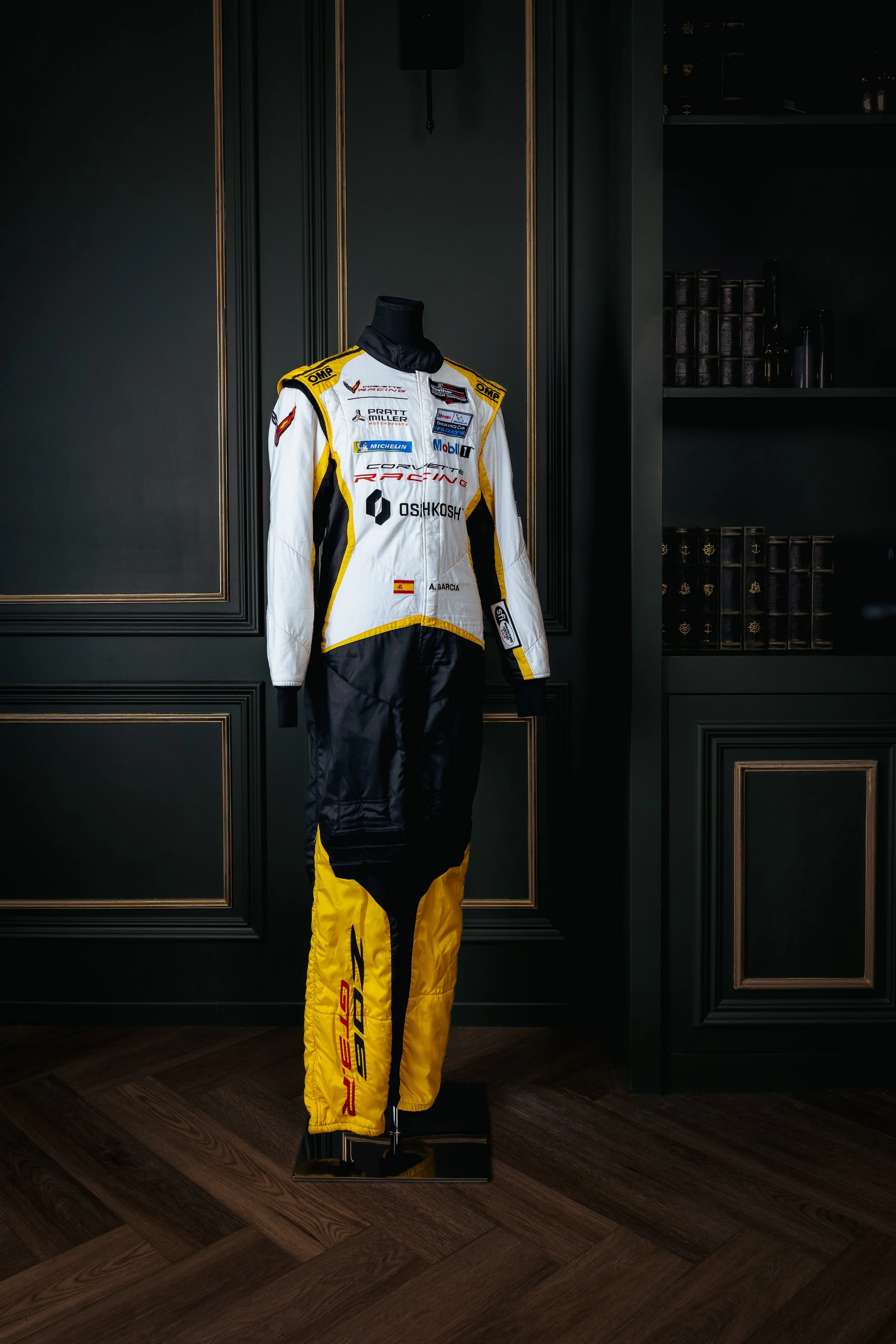 Racing suit displayed on a mannequin in a dark room with black paneled walls.