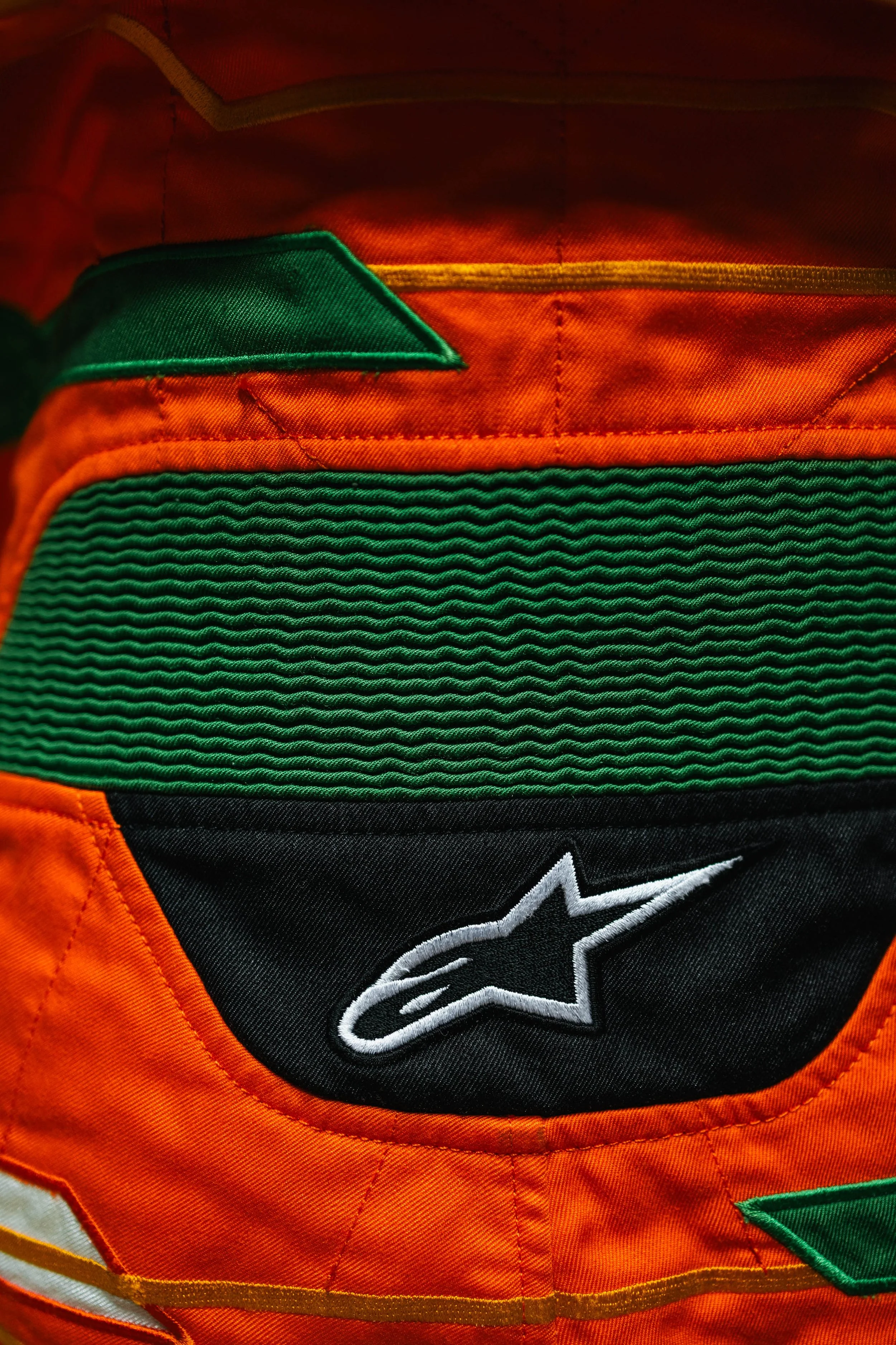 Close-up of an orange and black sports backpack with a green textured pocket and an embroidered white and black star logo.
