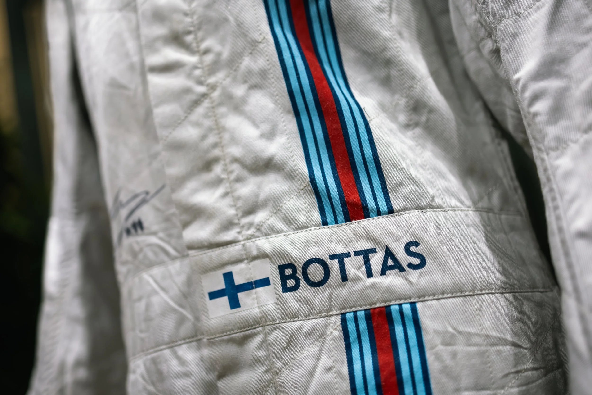 Close-up of a white racing suit with blue and red stripes, and a name tag reading 'BOTTAS' with a Finnish flag.