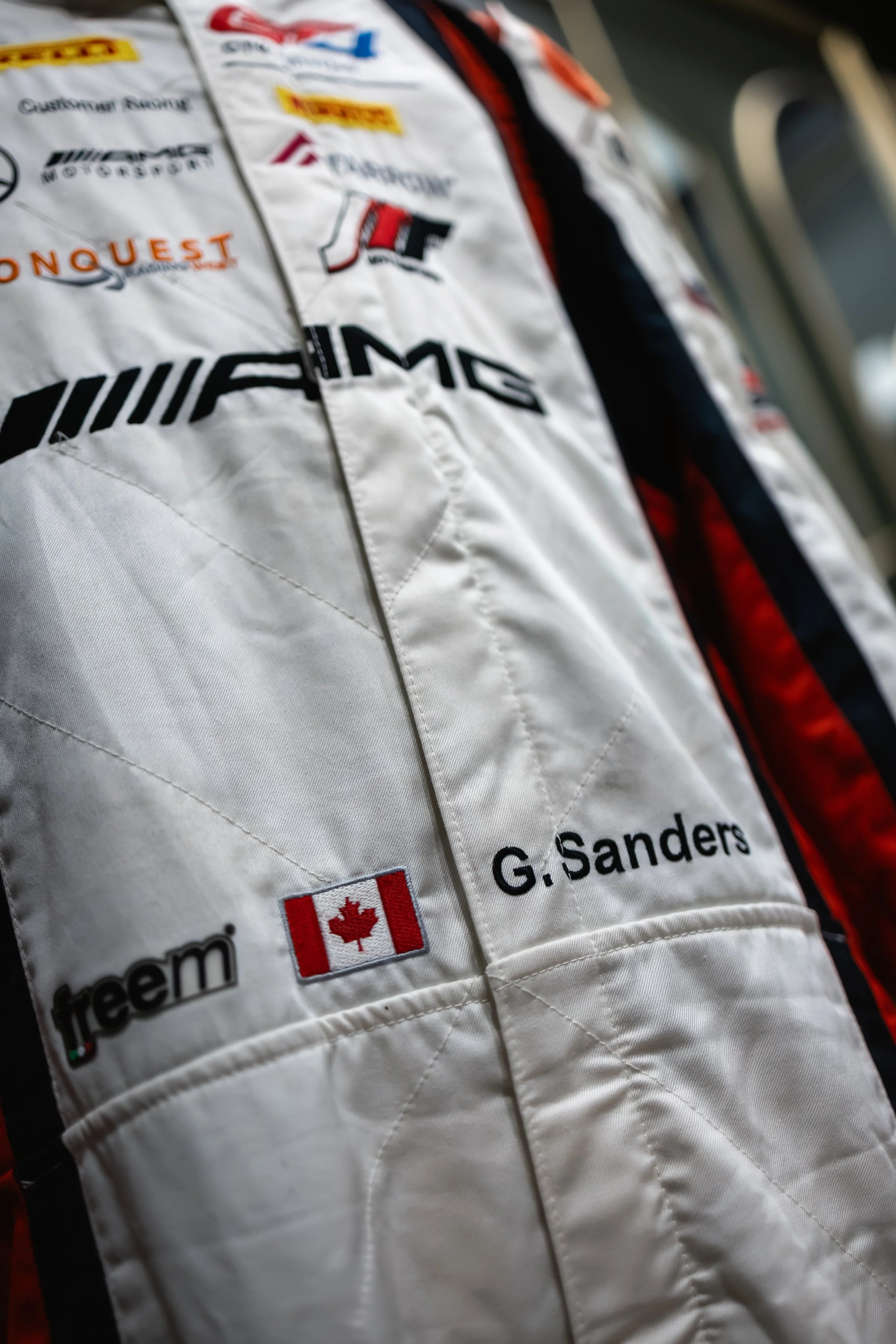 Close-up of a racing suit with sponsor logos, a Canadian flag, and the name G. Sanders embroidered on it.