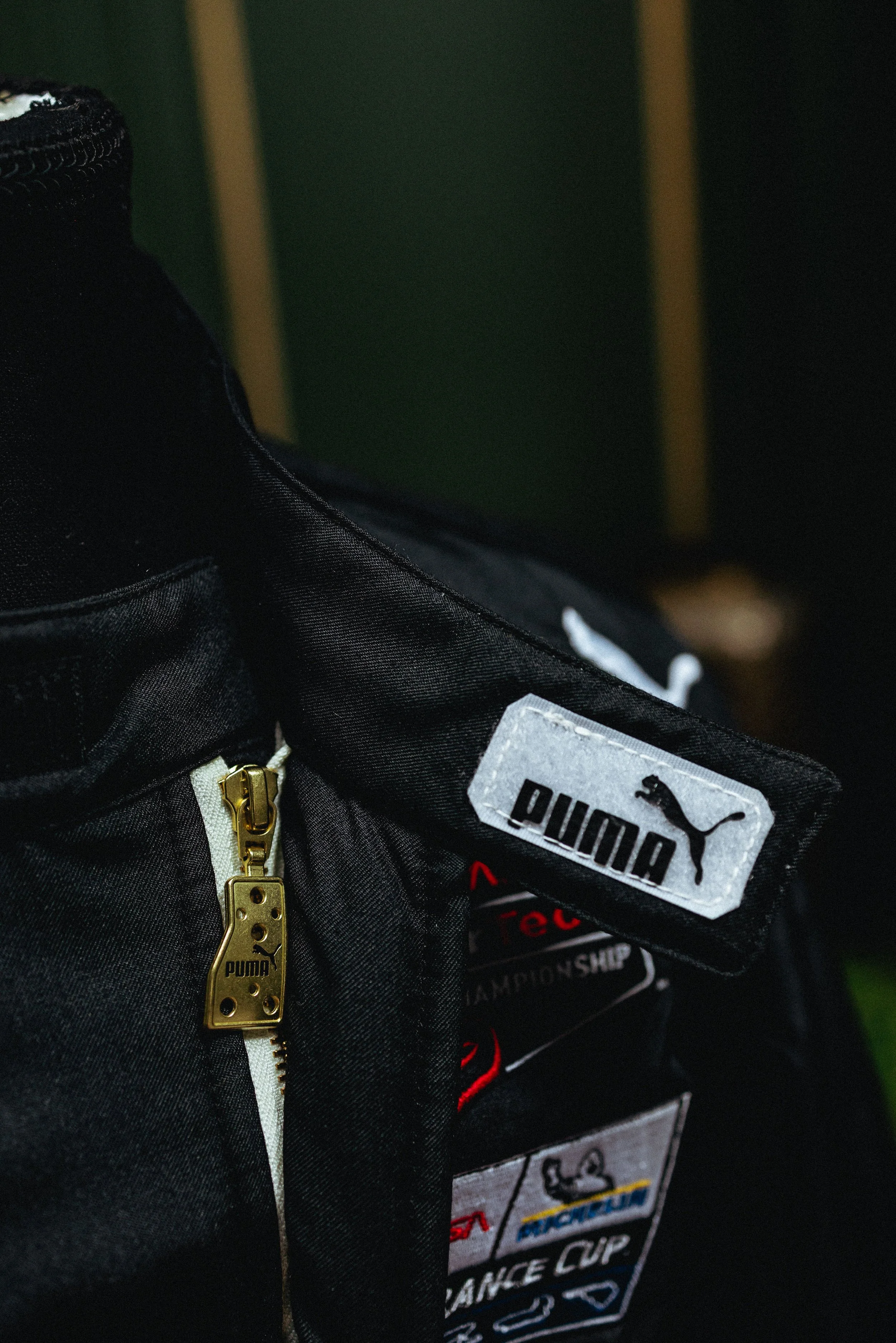Close-up of a black Puma sports bag with a gold zipper and several patches, including a Puma logo and event details.