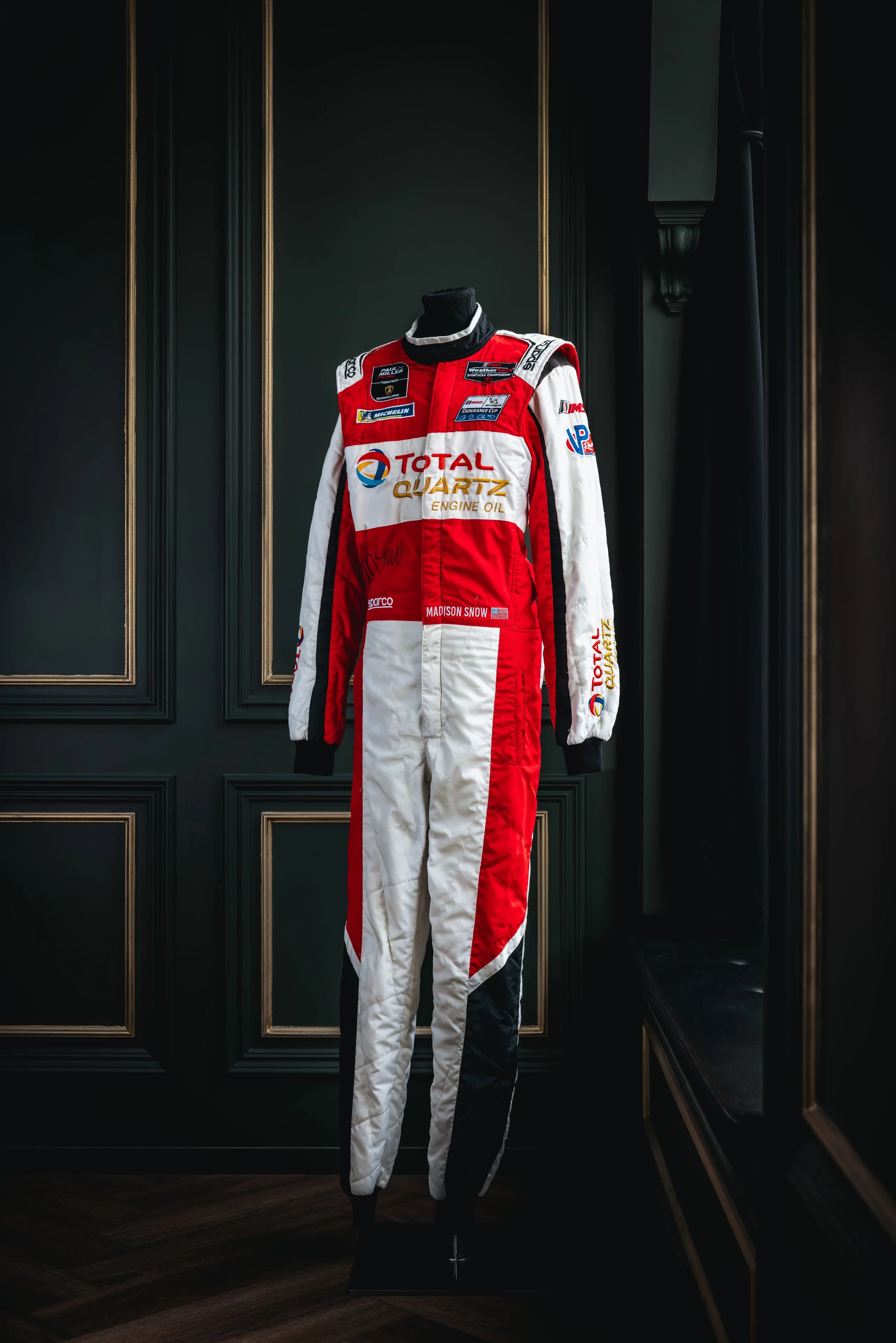 A racing suit displayed on a mannequin in a dimly lit room with dark green walls and gold accents.