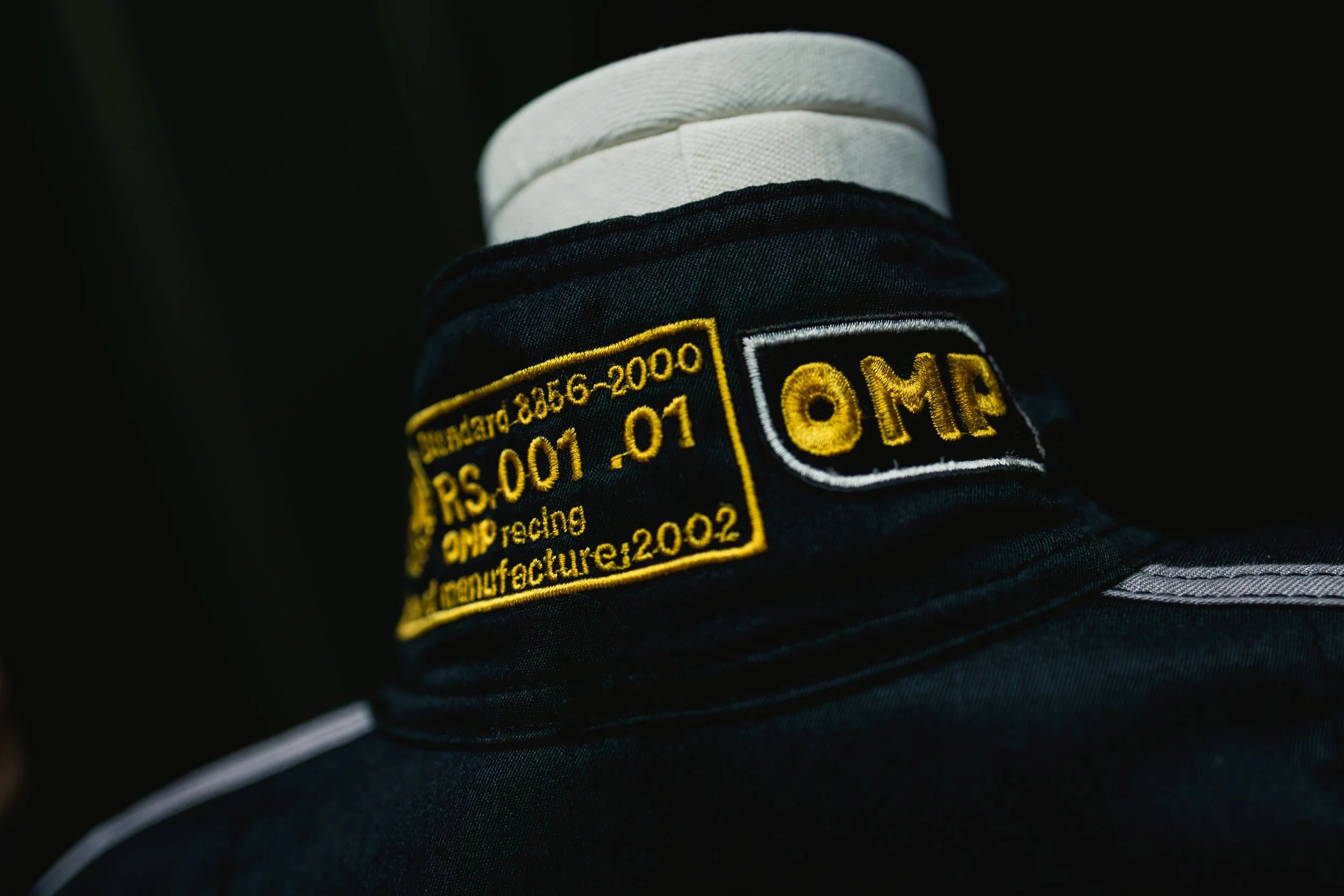 Close-up of a black jacket with a zipper that has a yellow "Orrlo" tag. Part of an embroidered patch or logo is visible on the jacket.