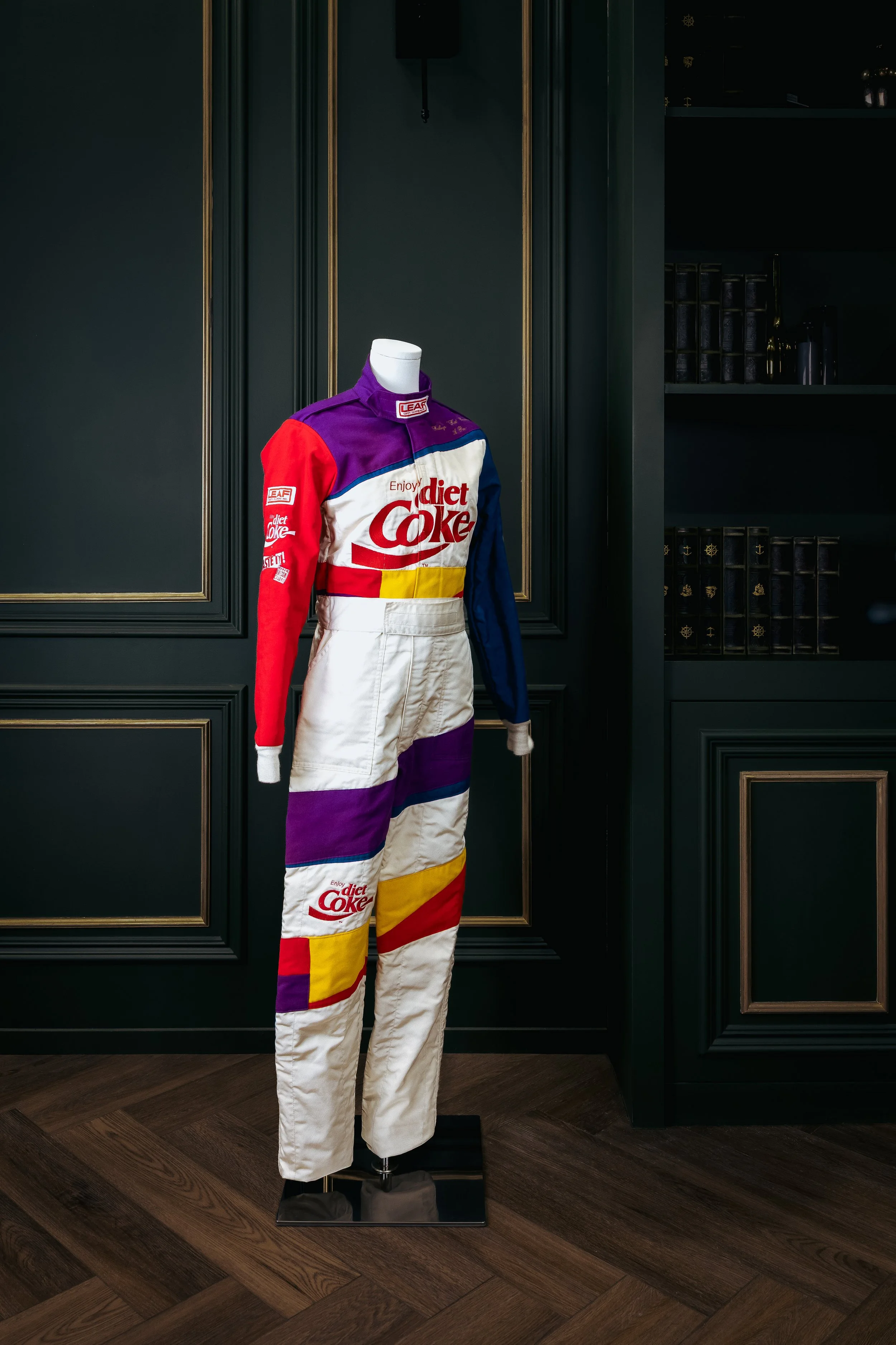 A racing suit on a mannequin featuring logos of Diet Coke and Enjoy.