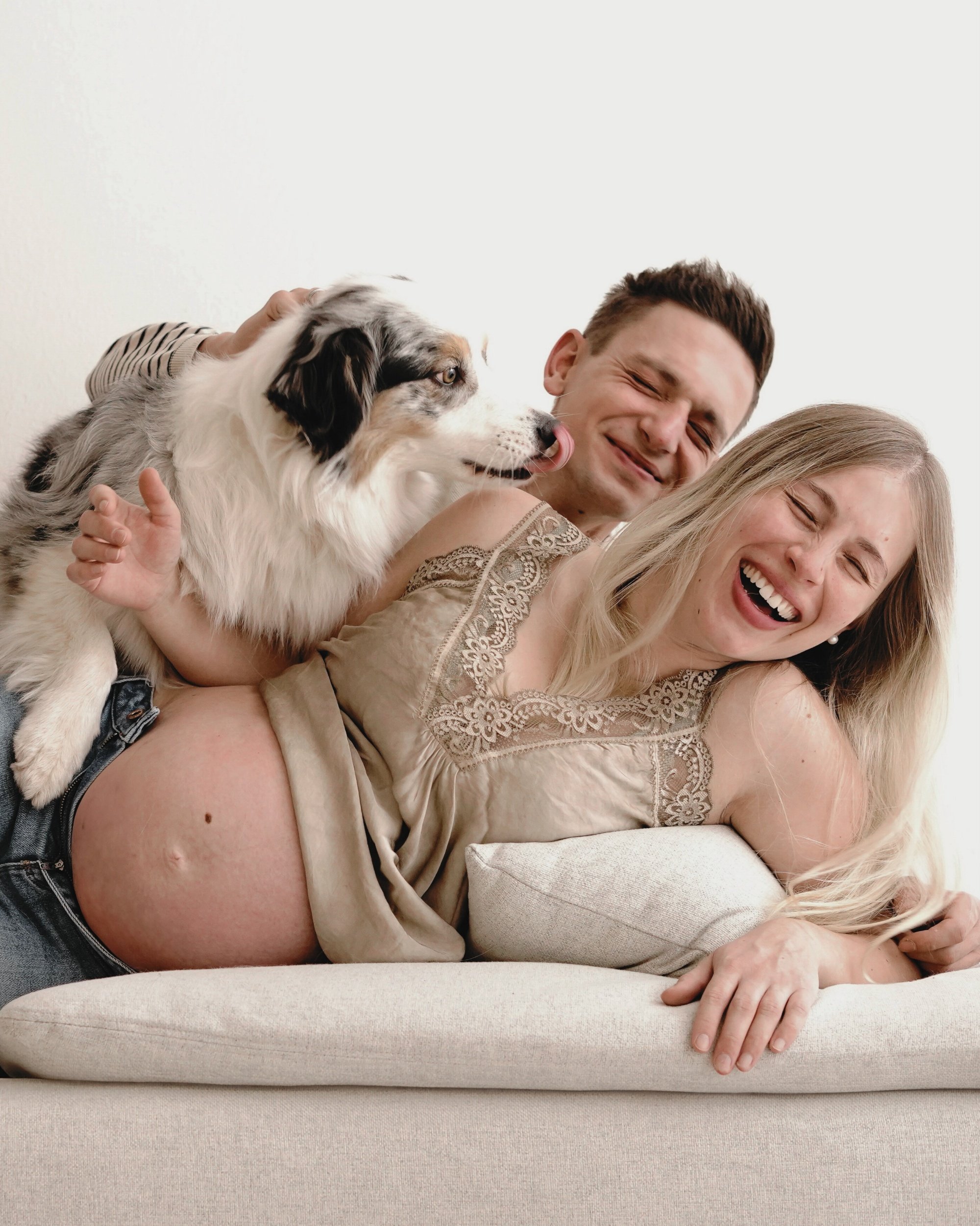 Ein lachendes Paar mit einem Australian Shepherd bei einer fröhlichen Kuschelzeit im Wohnzimmer.