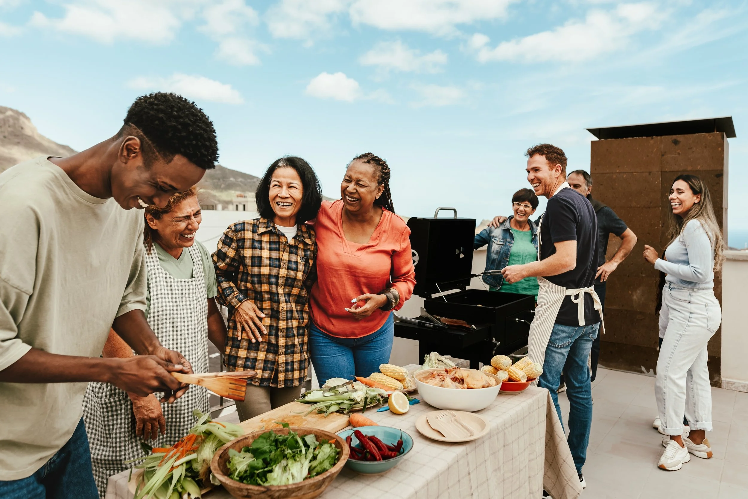 Group of friends having a barbecue on a rooftop, surrounded by food and smiling