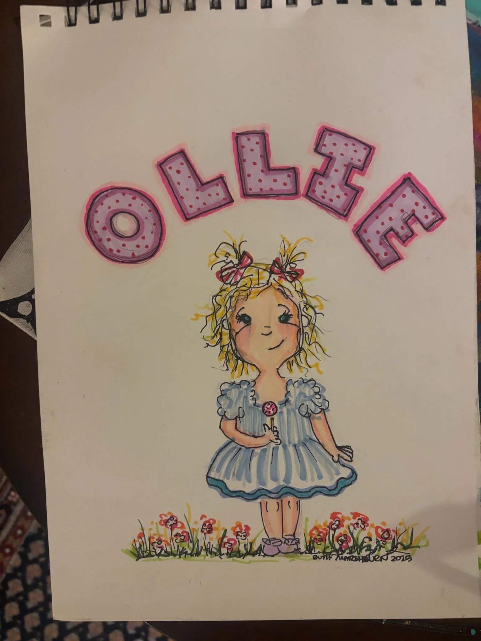 Colorful drawing of a girl with curly hair in pigtails, wearing a striped dress, holding a lollipop, standing on grass with flowers, with the name 'OLLIE' in large pink letters above her.