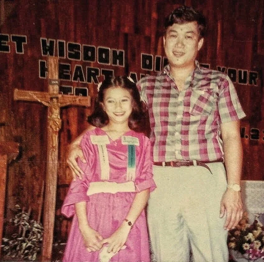 Childhood photo of Isabella standing beside her father with his arm around her. Both are smiling for the camera. The photograph accompanies a Father's Day essay about the greatest gift he gave her: the freedom to become herself.