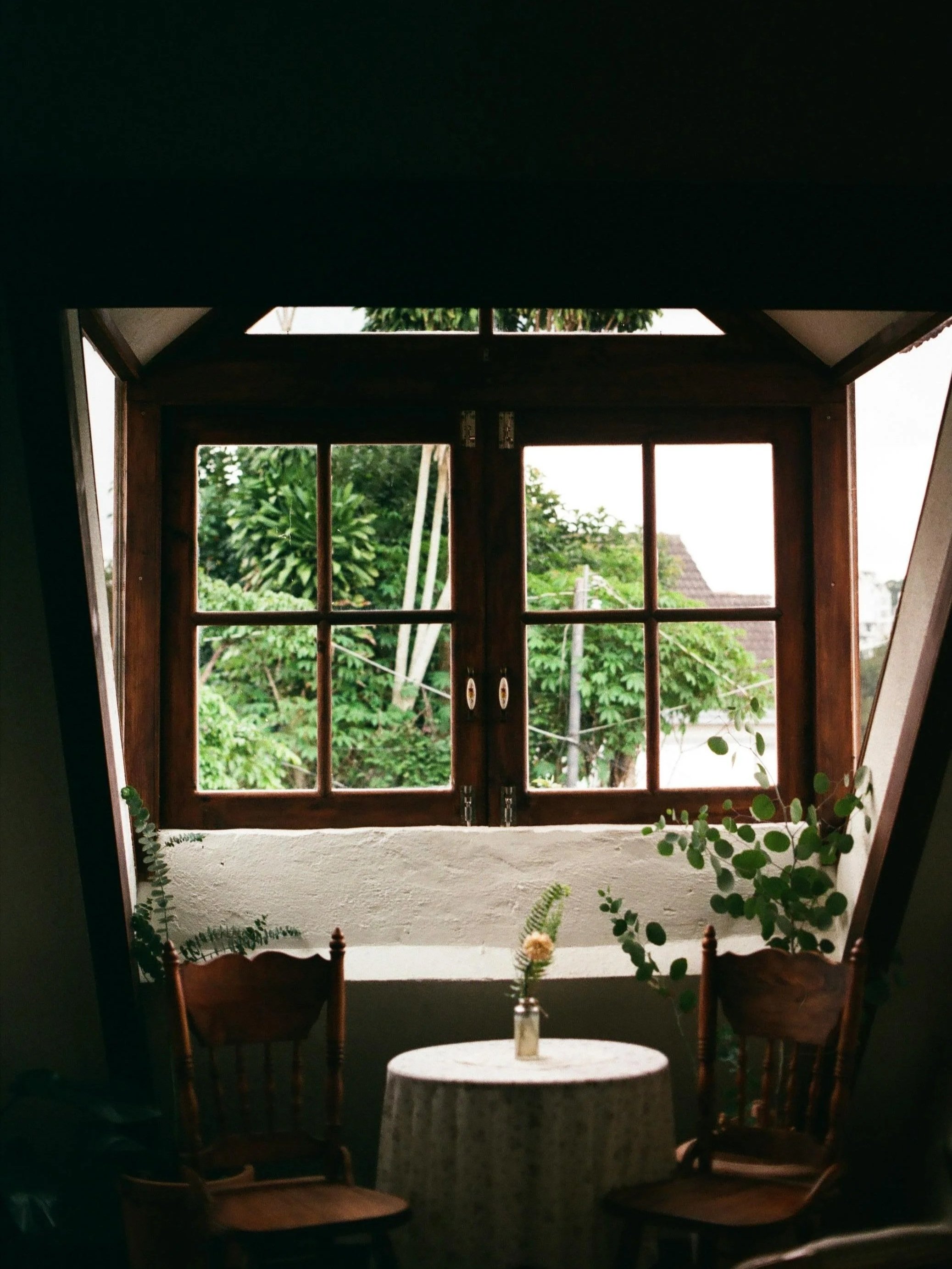 Softly lit therapy space with a wooden table, two chairs, and large windows overlooking greenery, evoking a calm, trauma-informed setting.