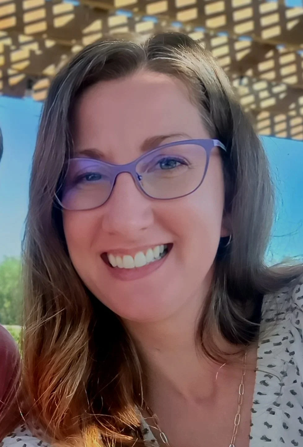 An image of the therapist, a middle-aged woman with long, wavy hair and glasses, who is smiling.