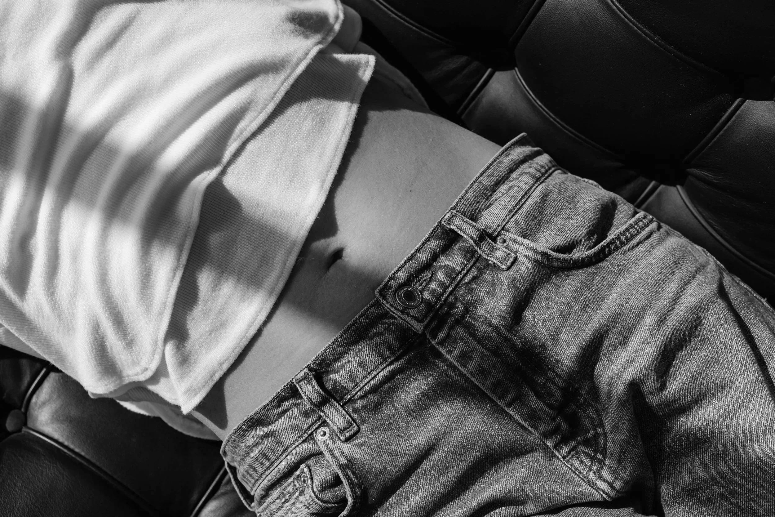 Close-up of a person lying down on a car seat, wearing a white shirt and ripped jeans, with part of their abdomen visible.