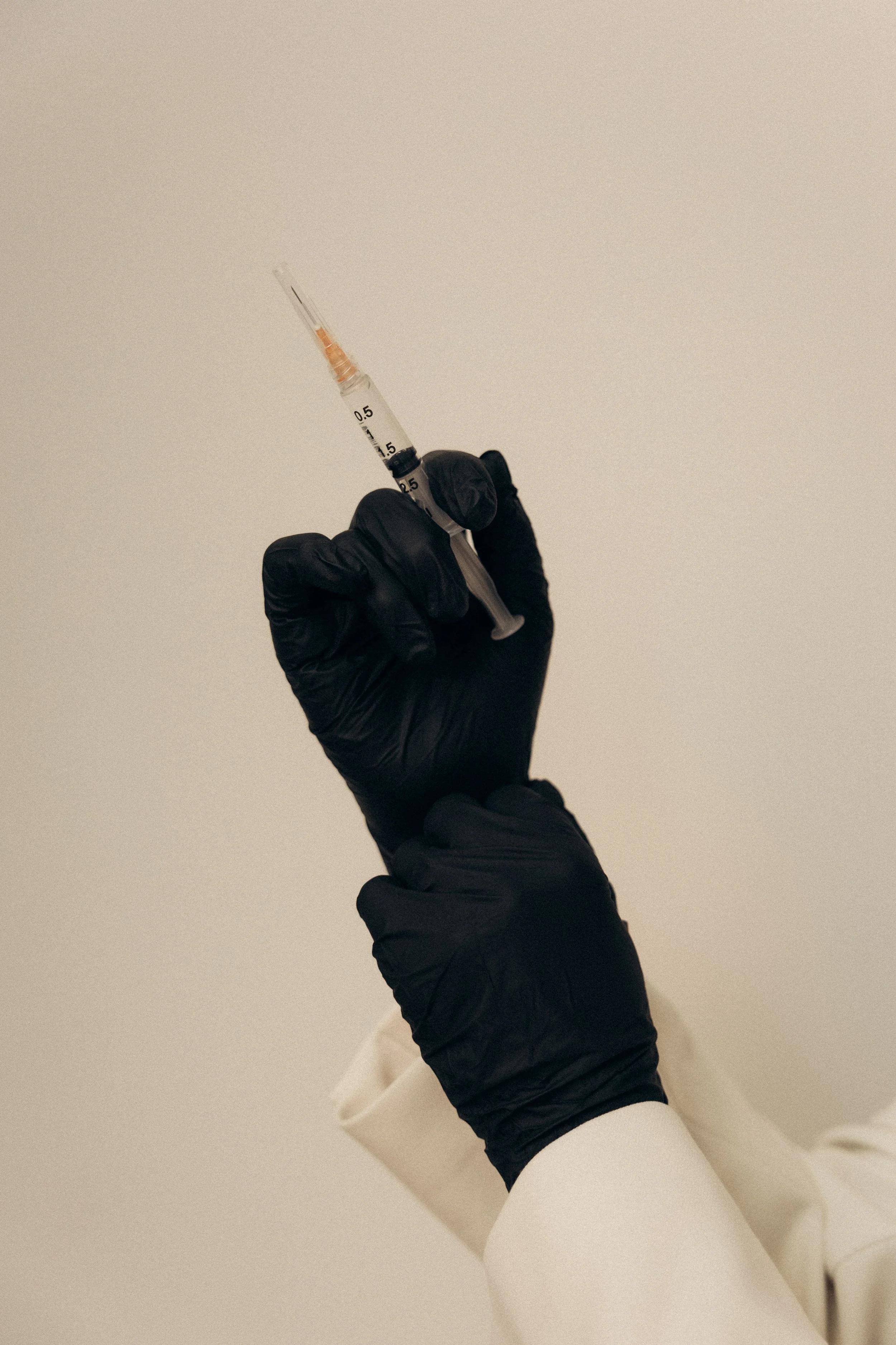 Close-up of a gloved hand holding a syringe with a needle, against a plain background.