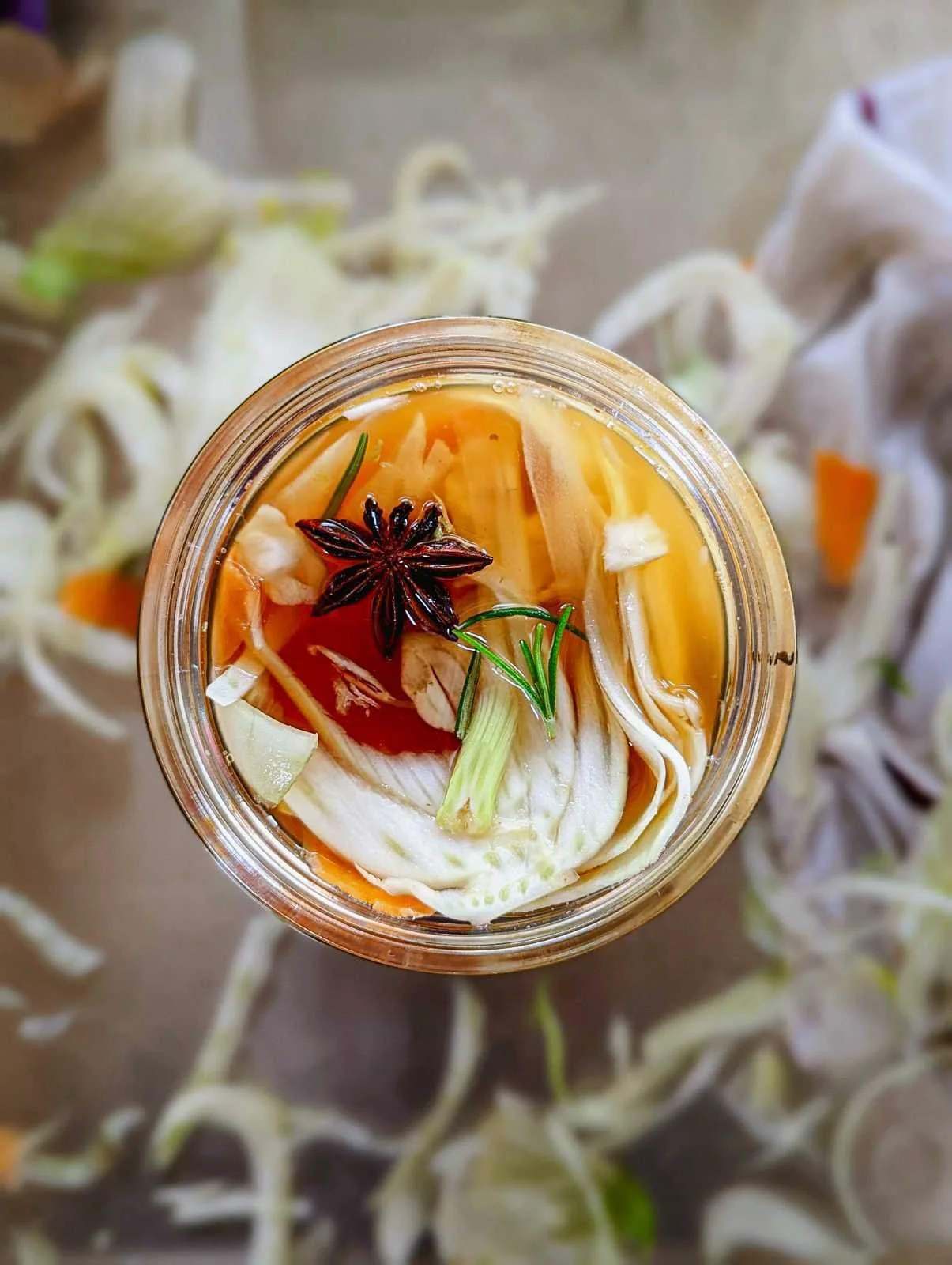 A top-down view of a jar of homemade vegetable broth with star anise, garlic, ginger, and green onion.
