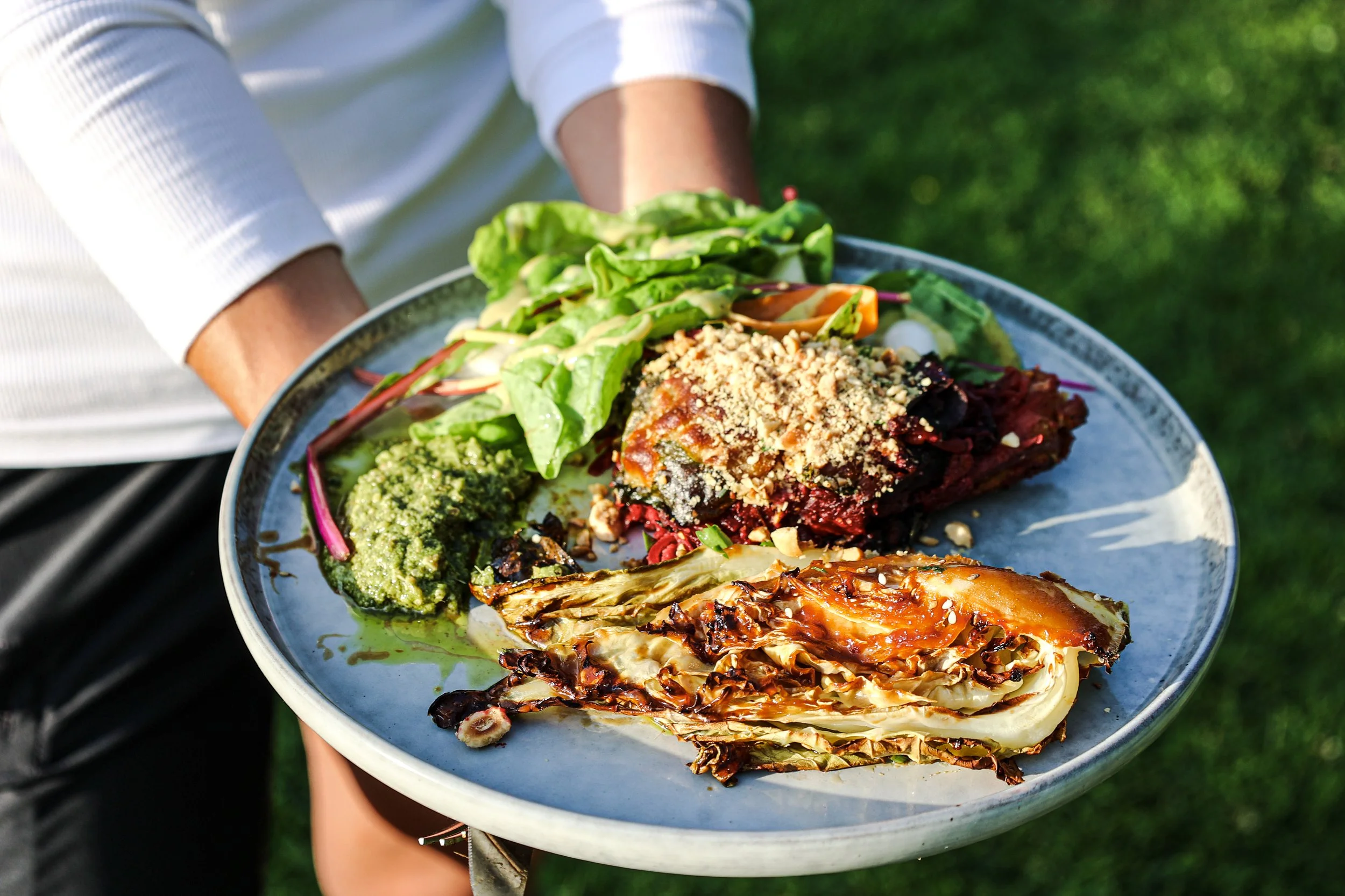 Person holding a large plate of grilled food and salad outside on green grass