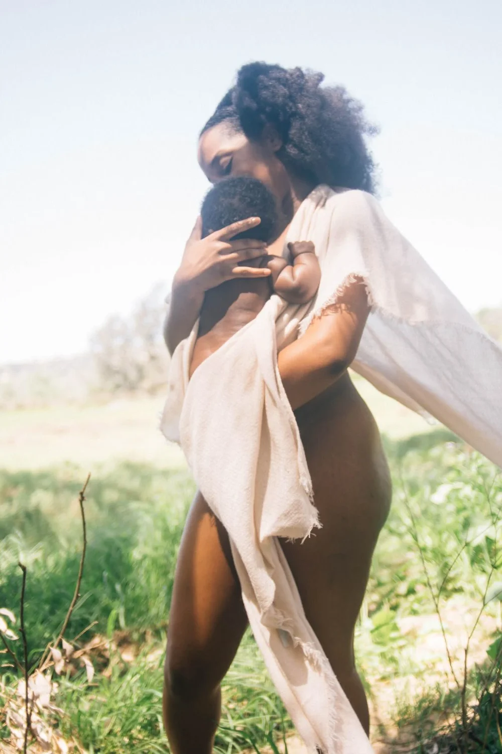 Mother holding her baby in linen in a field