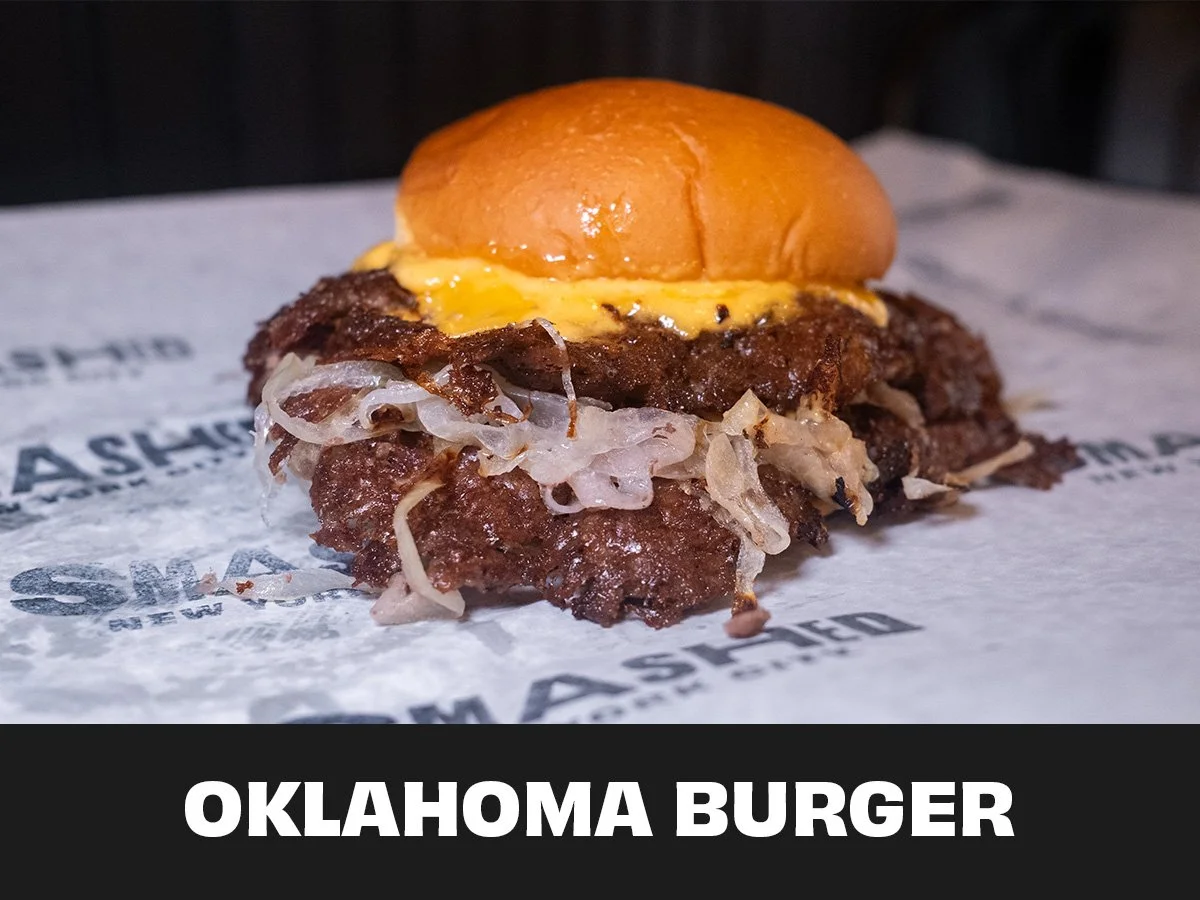 Close-up of an Oklahoma burger with a beef patty, topped with melted cheese and caramelized onions, inside a bun.