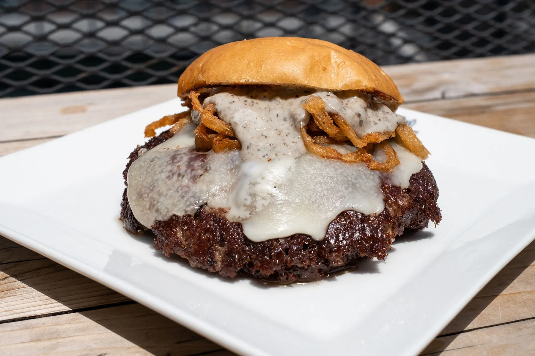 Cheeseburger with melted cheese, crispy fried onions, and a toasted bun on a white plate.